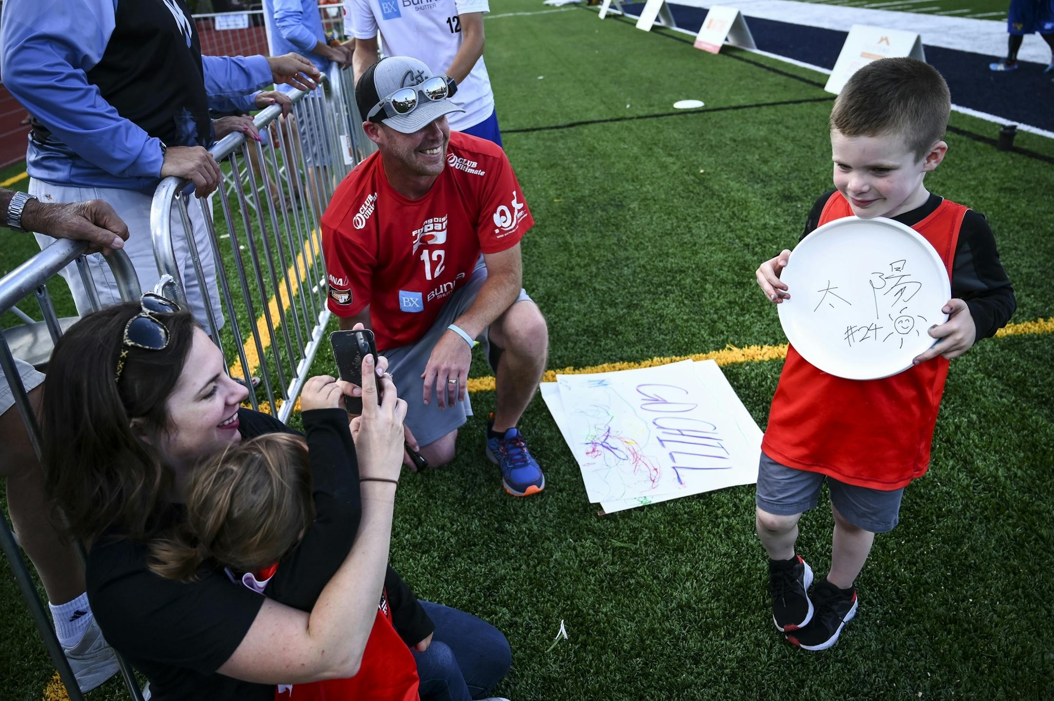 Jerika Owens held her daughter Charlotte as she took a photo of her son Henrik, 4, as he held a frisbee signed by the Buzz Bullets' game MVP Keiichero Shiba. In the middle knelt Todd Owens, former Wind Chill assistant coach.