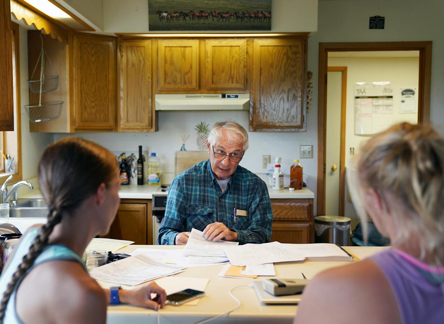 Bowman sifts through paperwork in his kitchen with sisters Laura, left, and Anne Johnson as they finalize the adoptions of several horses. The Johnsons, who work with Bowman, spent the day helping a family pick out potential barrel racers. Eight horses found new homes that weekend.