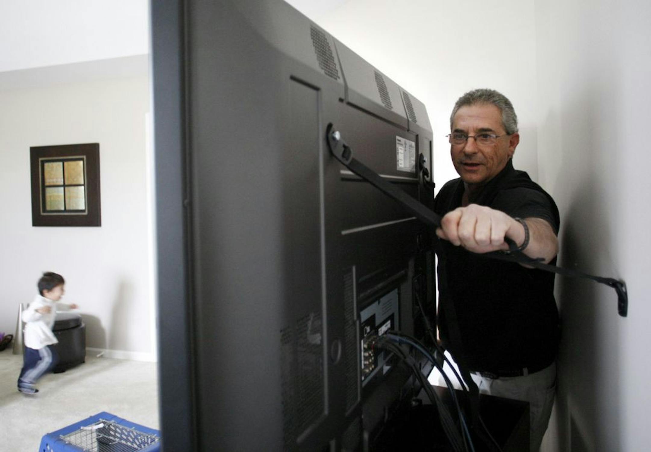 Arvey Levinsohn installs an anchor strap to a flat-screen television to keep it from tipping over on a child at a home in Westmont, Ill.