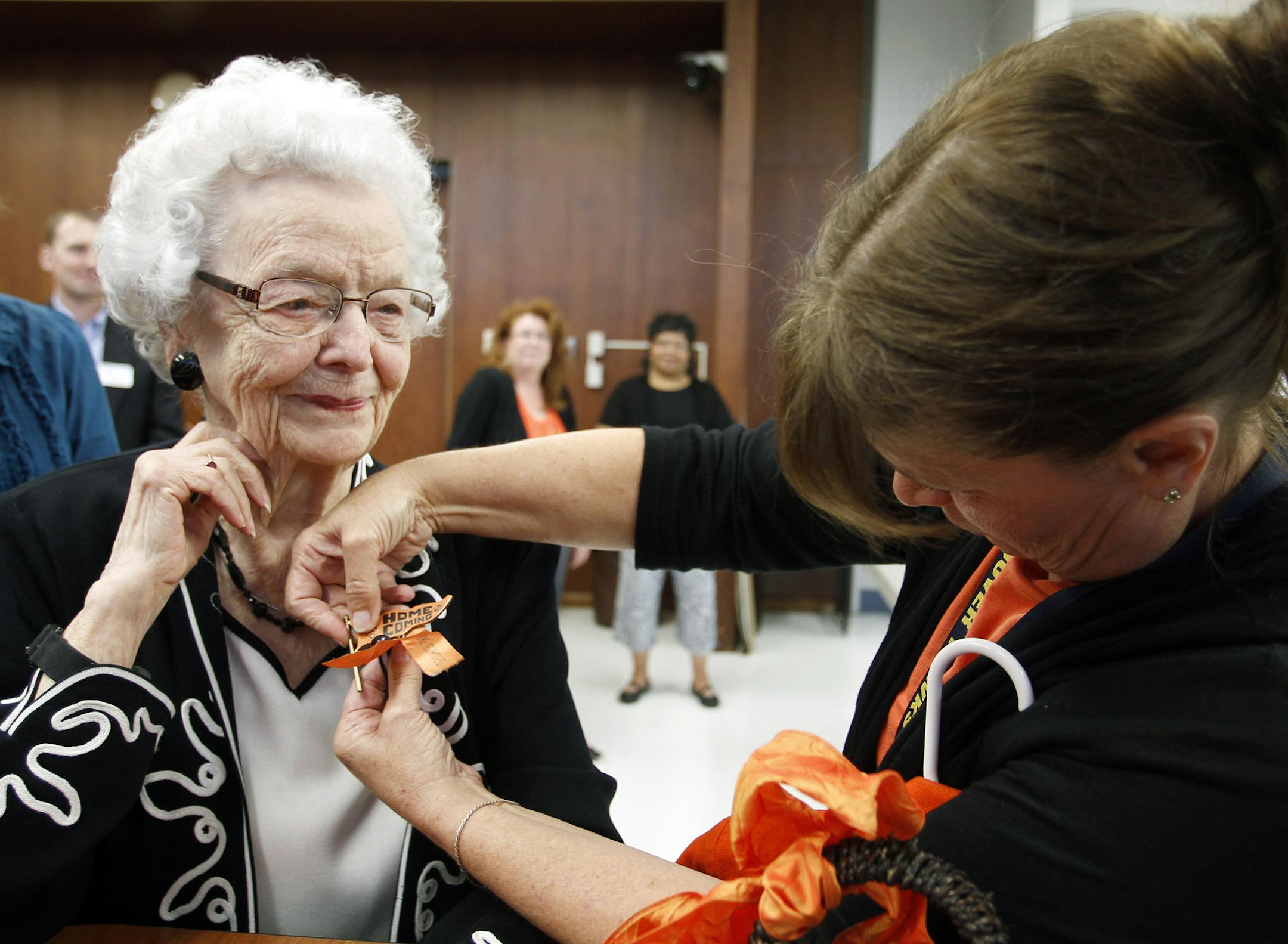 In this Sept. 23, 2013, Audrey Crabtree, 99, left, smiles as Sarah Dierks pins a 1972 East High homecoming pin onto her jacket during an during an education board meeting in Waterloo, Iowa, where she received an honorary diploma. Crabtree dropped out of a Waterloo high school in 1932 due to an injury and to care for her grandmother. She went on to run her own business for nearly three decades. (AP Photo/Waterloo Courier, Tiffany Rushing)