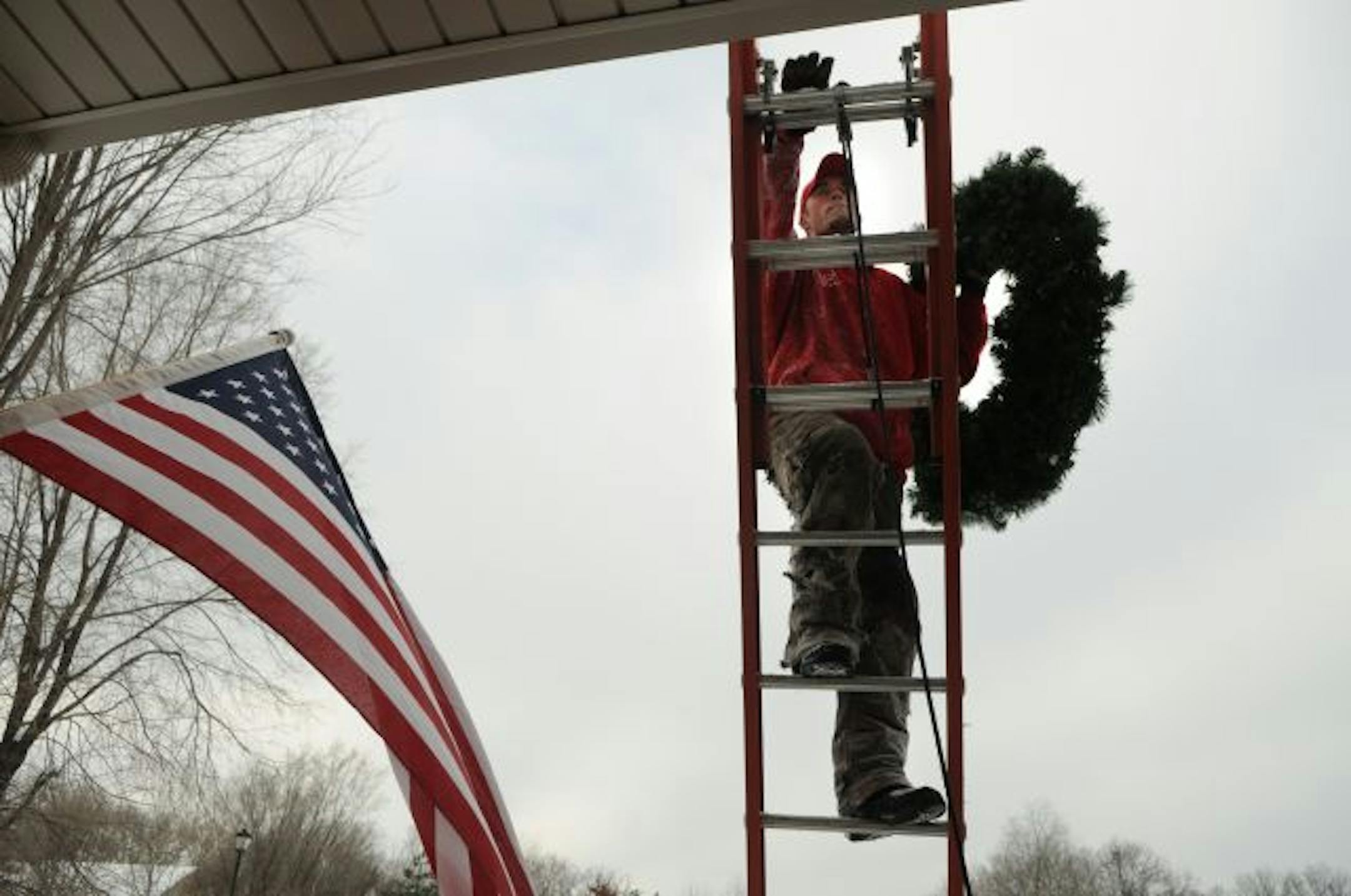 Jeremy Leonard hauls a wreath up a ladder as one of the finishing touches on the house lighting.