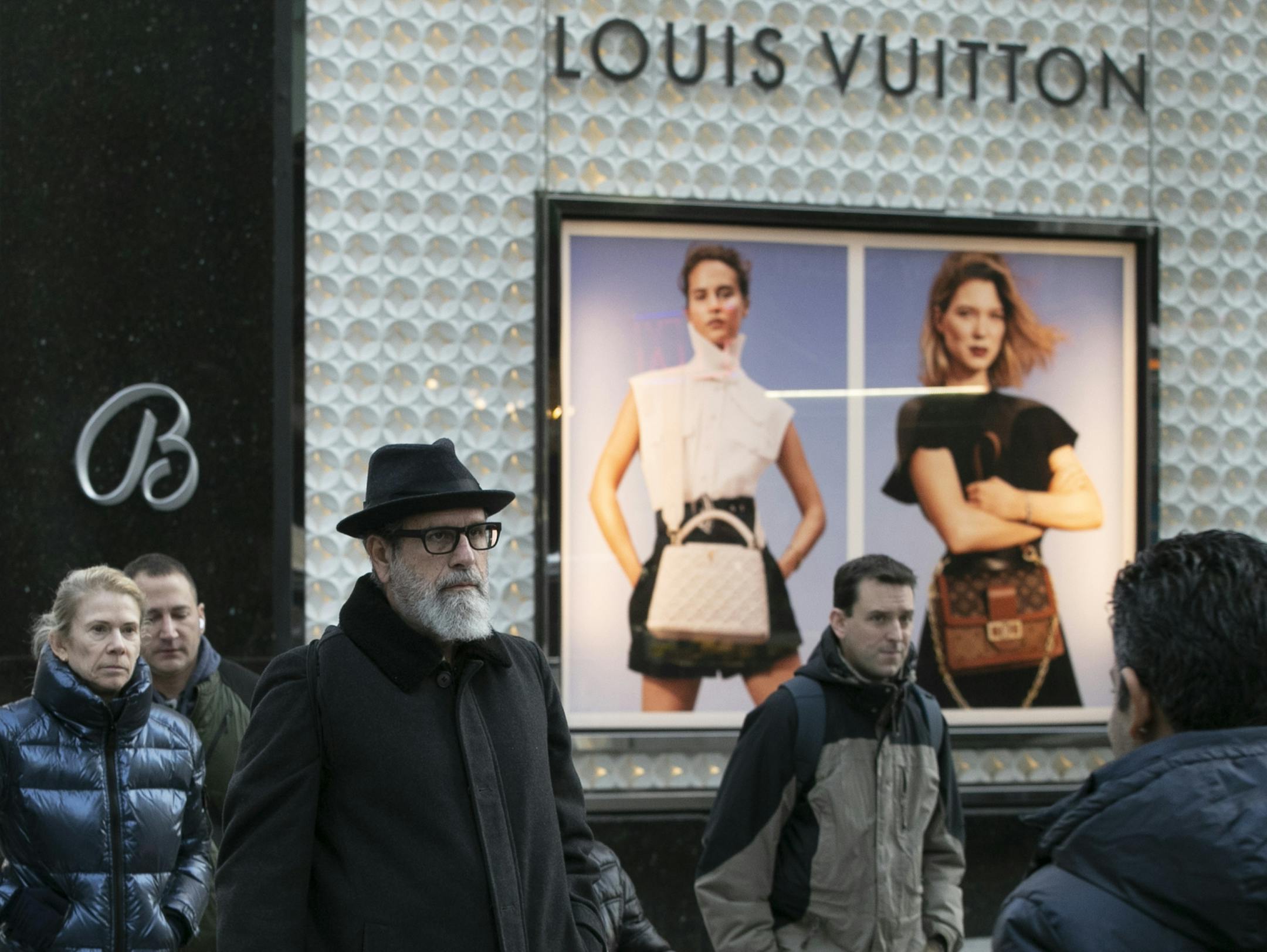 FILE - In this Nov. 25, 2019 file photo, pedestrians pass a store window for luxury brand Louis Vuitton, in New York. There are plenty of designer and luxury brands on the market, and in part because of Instagram's fashion bloggers and influencers, they're all the rage. Whether you want to invest in a quality item to last for years or you just want to treat yourself to a luxury label every once in a while, you can reduce your costs by shopping secondary markets or outlet stores. (AP Photo/Mark L