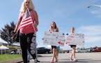 Crissy Essex, left, 44, Sabrina Cupell, and Cheyenne Essex bring signs and an American flag to a memorial near where a gunman fired shots into the Arm