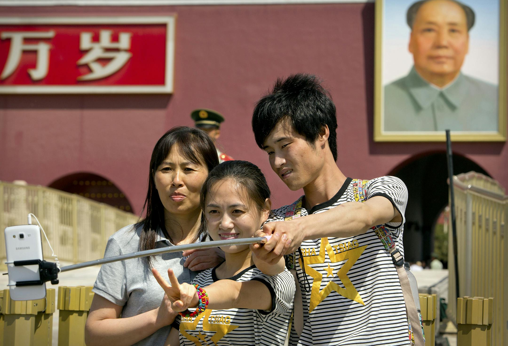 Tourists use a selfie stick to take a photo of themselves in front of a large portrait of late Chinese leader Mao Zedong on the Gate of Heavenly Peace near Tiananmen Square in Beijing, Sunday, May 3, 2015. Millions of Chinese are taking advantage of the May Day holidays to visit popular tourist sites. (AP Photo/Mark Schiefelbein) ORG XMIT: XMAS101