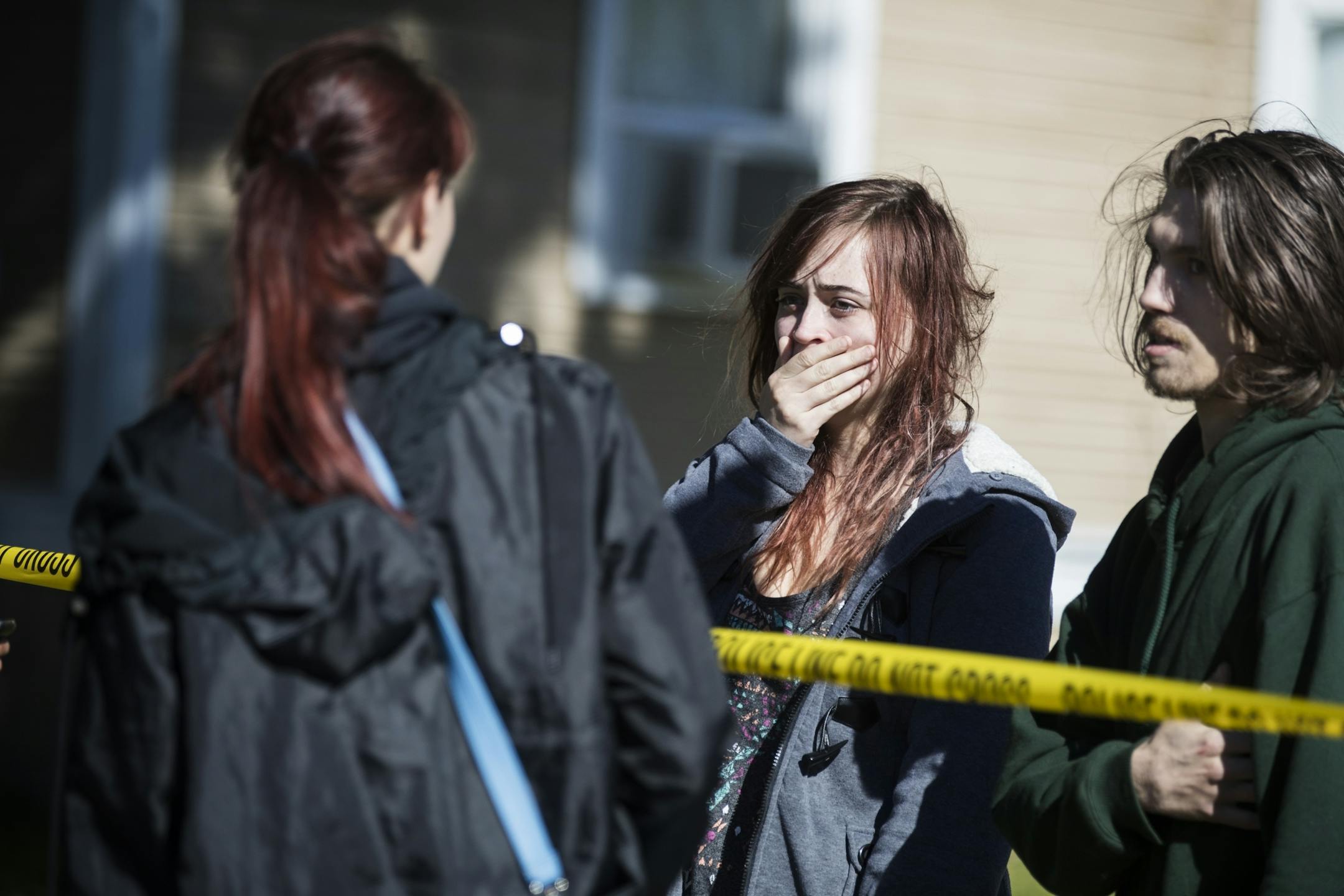 Potential witnesses stand behind the police tape, waiting to be questioned by the police.