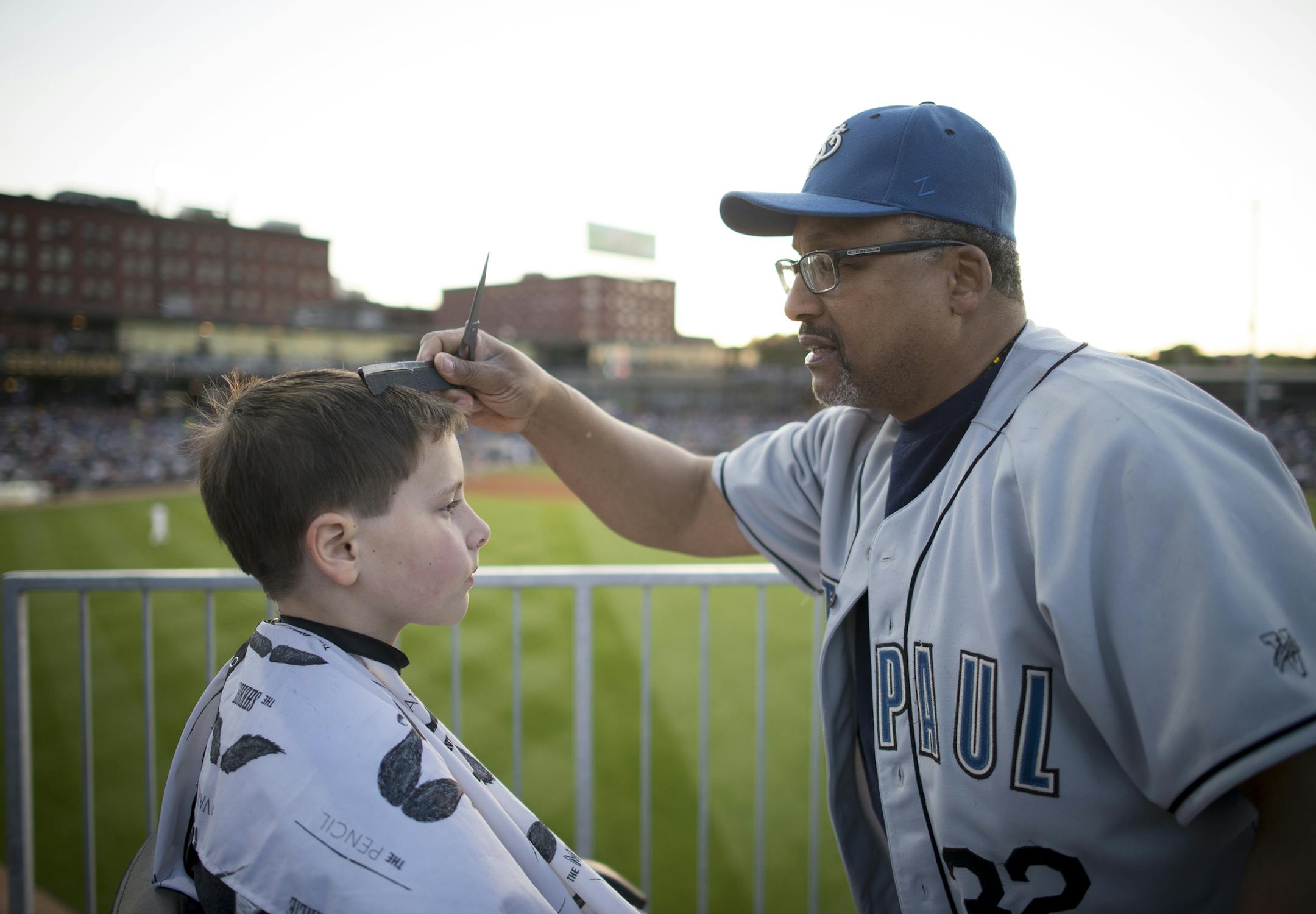 Barber Bilal Salem cut the hair of Maxwell Cronk, 10, in the outfield during Thursday night's game. ] Aaron Lavinsky &#x2022; aaron.lavinsky@startribune.com The St. Paul Saints hold their season opener against the Fargo-Moorhead Redhawks at brand-new CHS Field on Thursday, May 21, 2015.