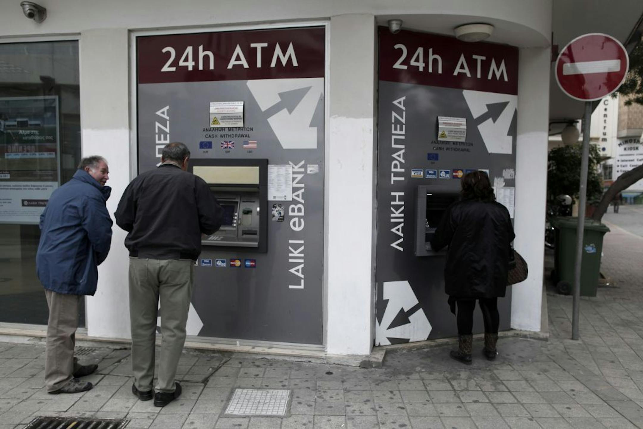 Cypriots use the ATM machines outside of a closed Laiki Bank branch in capital Nicosia, Cyprus, Tuesday, March 19, 2013. Cypriot finance officials are revising a planned financial bailout to relieve small account holders from having to pay a charge on their savings in order to secure an international rescue of the country's troubled banks.