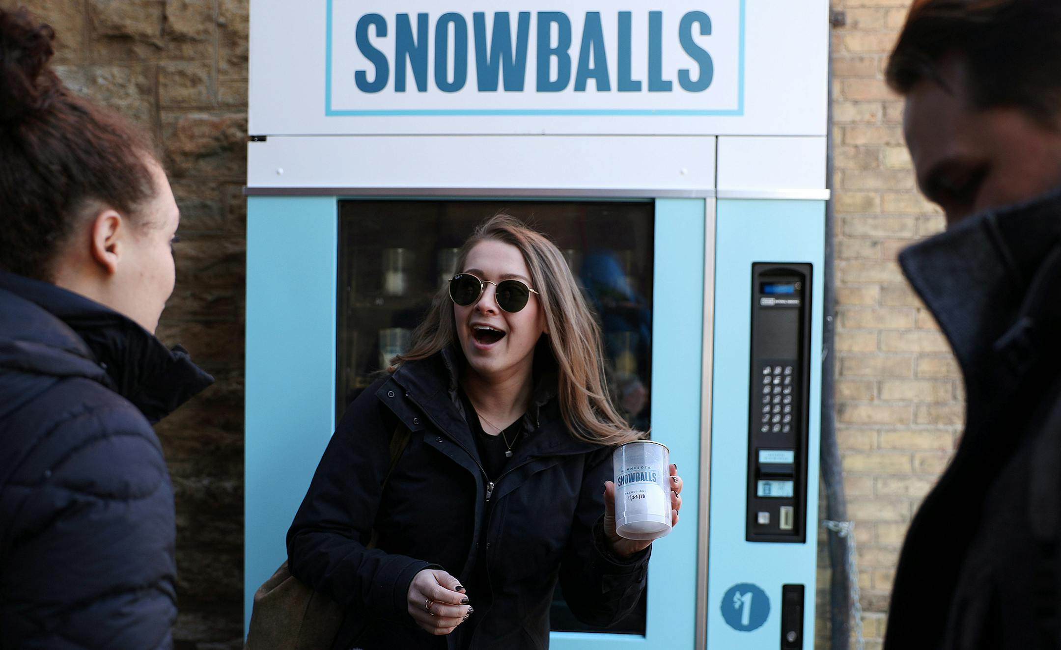 Brianna Sudrla, center, of Chicago reacted after buying a "real Minnesota snowball" for $1 from a vending machine in the alley behind the Hewing Hotel. Also pictured is Slyssa Raiola, left, of Minneapolis and Beau Lemire of Chicago. ] ANTHONY SOUFFLE ï anthony.souffle@startribune.com The first-ever (known) snowball vending machine - a machine that sells real, hand-packed snowballs to Super Bowl visitors - attracted customers who purchased them for $1 Thursday, Feb. 1, 2018 in the North Loop
