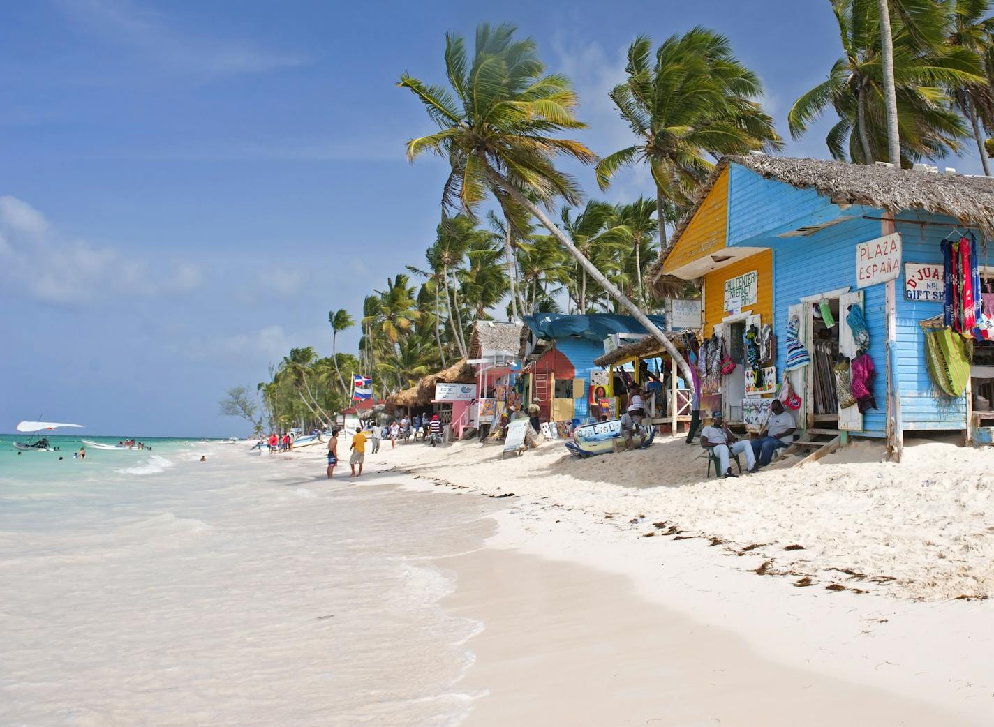 Punta Cana, Dominican Republic- July 20, 2013: Tourist walking on the beach and take a tour of the bungalows-stalls with souvenirs. Locals sitting in front of stalls