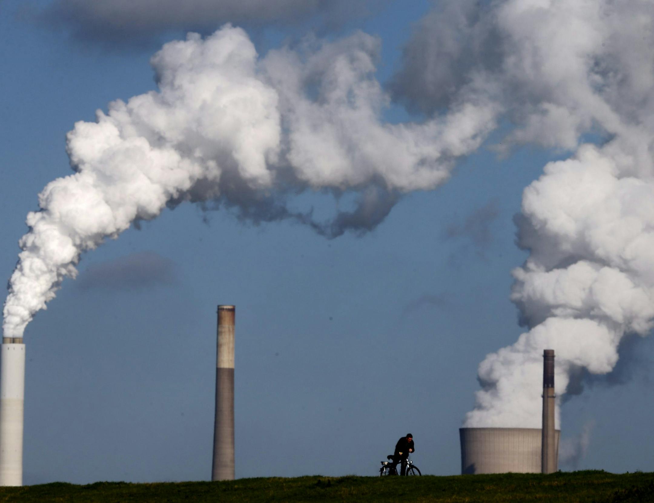 FILE - The Oct. 24, 2013 file photo shows a cyclist passing steaming chimneys on the river Rhine bank in Duisburg, Germany. Europe got more bad news about its dominant economy Tuesday, Oct. 14, 2014 when the German government slashed its growth estimates for this year to 1.2 percent from 1.8 percent. The cut follows a run of disappointing data on exports, industrial production and factory orders ó the heart of Germany's manufacturing and export-dominated economy. The drip, drip of bad news