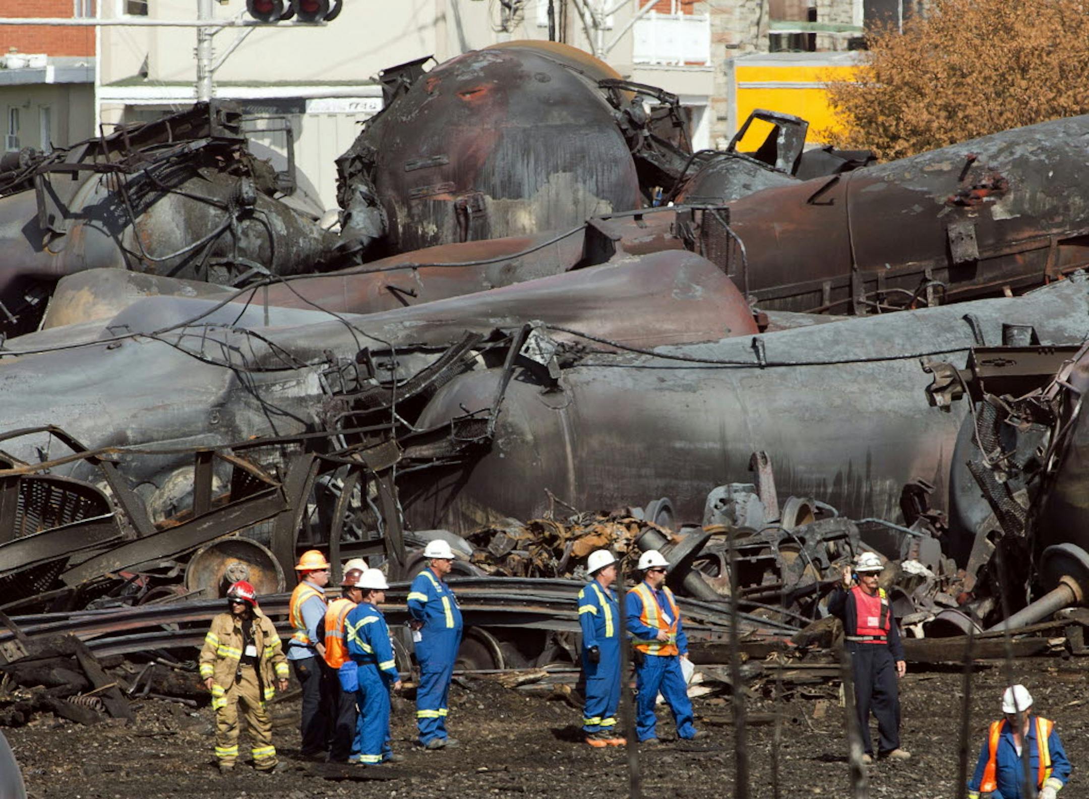 Workers stand before mangled tanker cars at the crash site of a train derailment and fire in Lac-Megantic, Quebec, that happened on July 6, 2013.