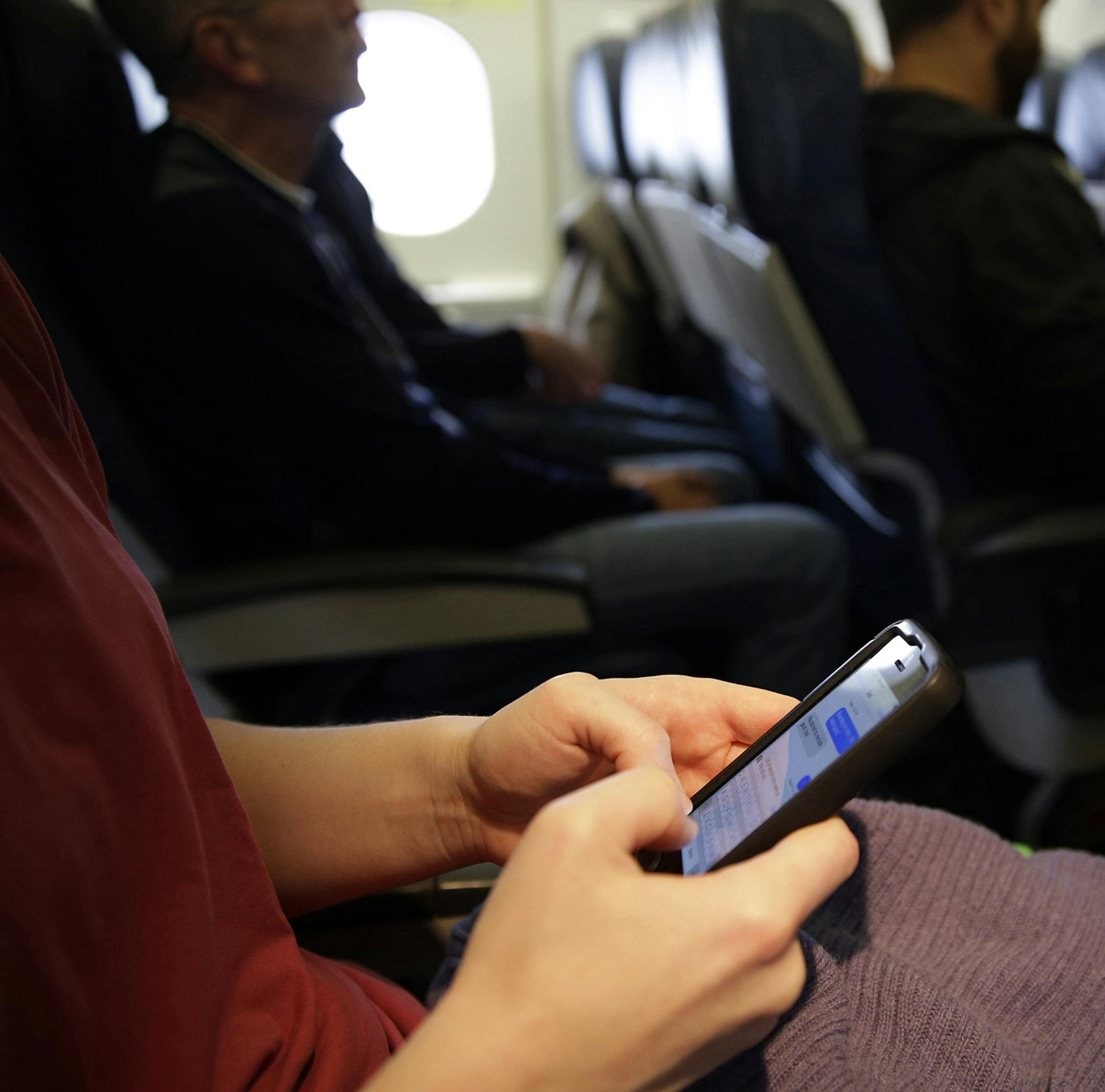 FILE - In this Oct. 31, 2013, file photo, a passenger checks her cell phone before a flight in Boston. The Federal Communications Commission might be ready to permit cellphone calls in flight. Old concerns about electronics being a danger to airplane navigation have been debunked. And carriers could make some extra cash charging passengers to call a loved one from 35,000 feet. But that extra money might not be worth the backlash from fliers who view overly-chatty neighbors as another inconvenien