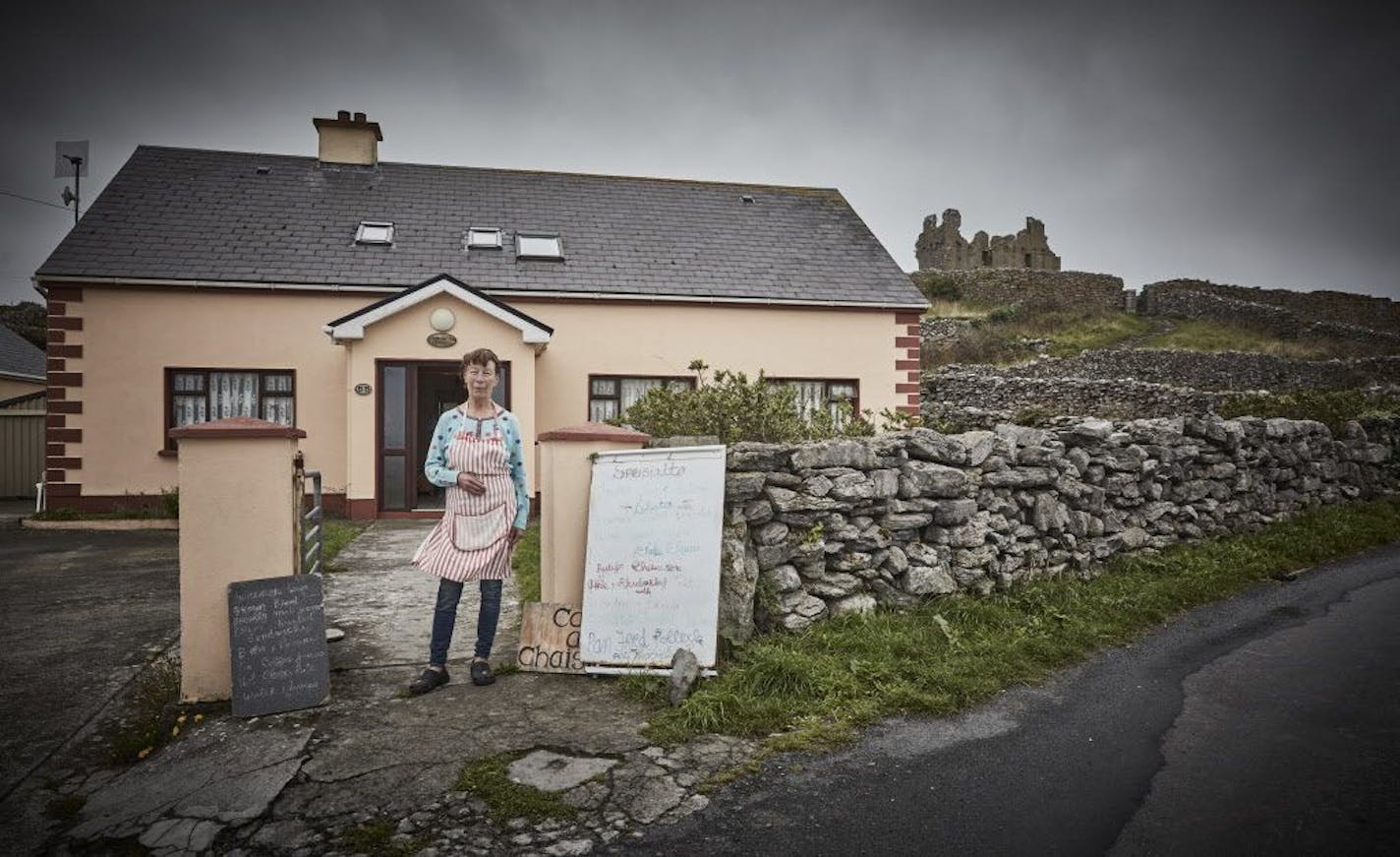 Aine O'Graiofa outside her home and restaurant, with O'Brien's Castle in the background, on Inisheer, County Galway, Ireland, July 2018. Just as in the days of J.M. Synge, who wrote his celebrated plays there, the Aran Islands can feel like a place lost in time.