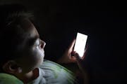 Teen looking at cellphone in dark room.