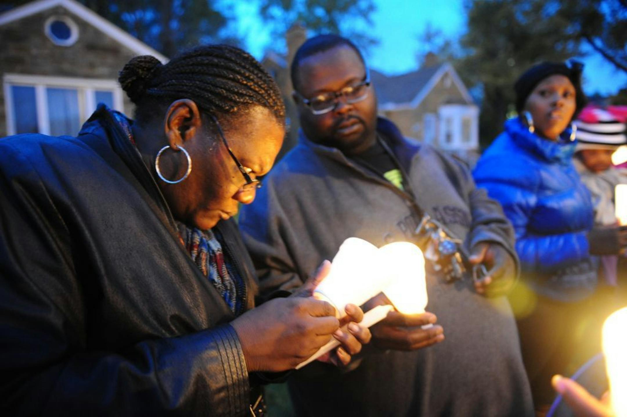 In this Wednesday, Nov. 6, 2013 photo, Charles Hannah lights Theresa Walker's candle, left, at a candlelight vigil for Renisha McBride in the front of the home where she was shot in Dearborn Heights, Mich.
