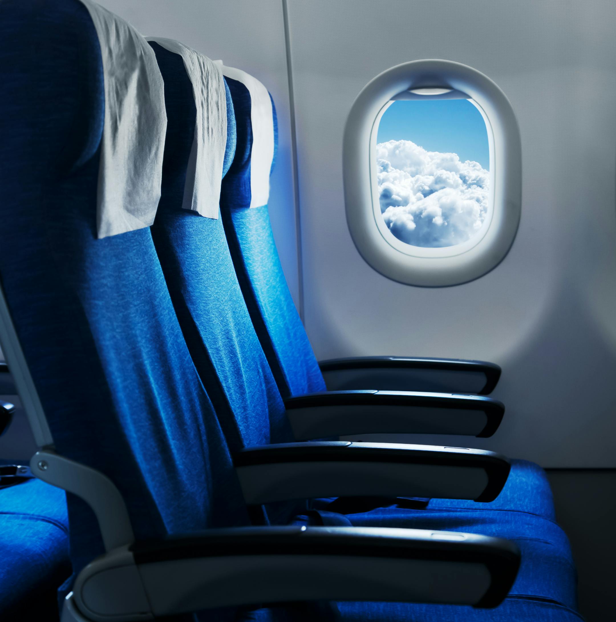 Empty air plane seats. Blue sky and clouds in the window. Airplane interior