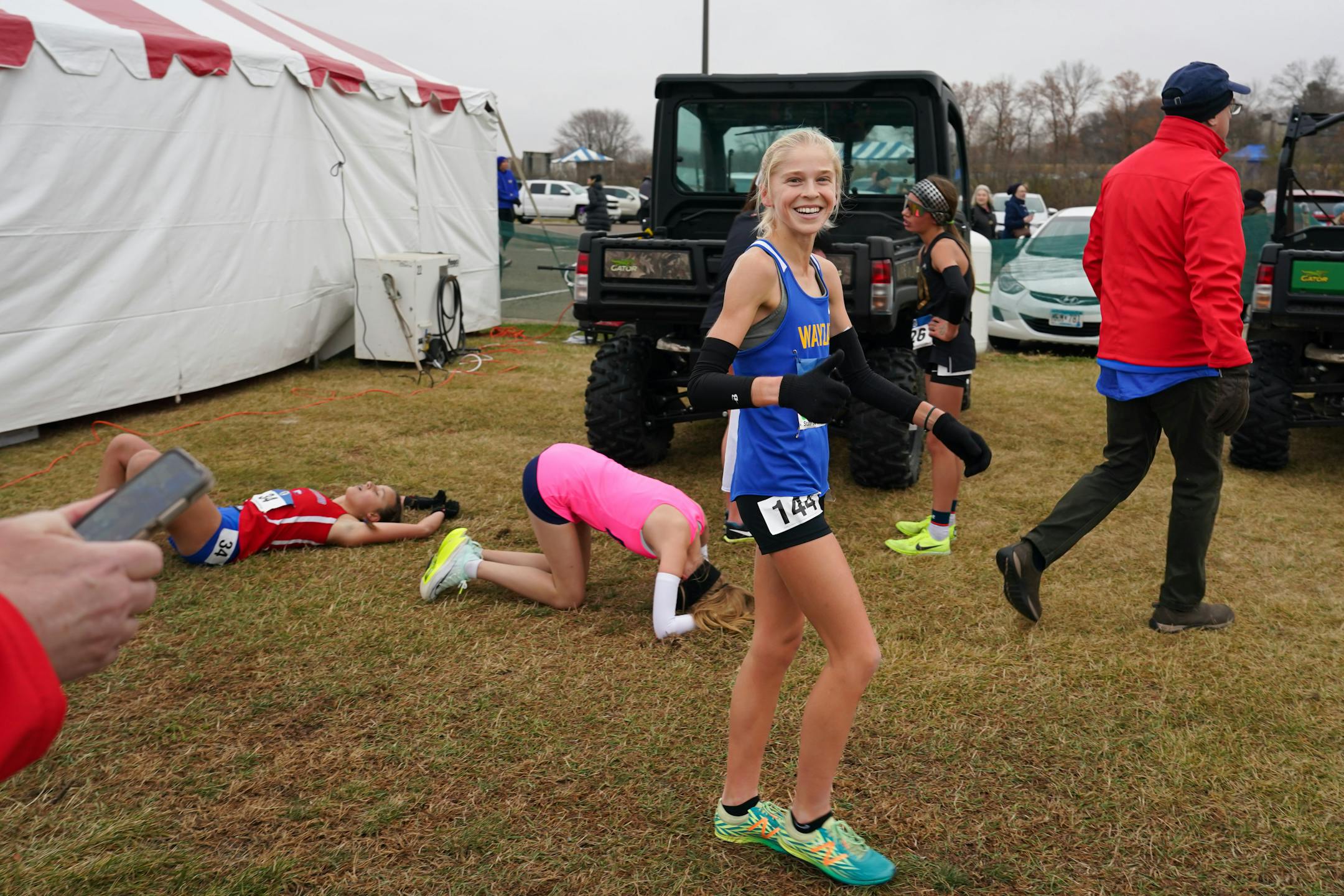 With collapsed competitors around her, Abbey Nechanicky of Wayzata givers the thumbs up after crossing the finish line with a time of 16:47.61 winning the race.