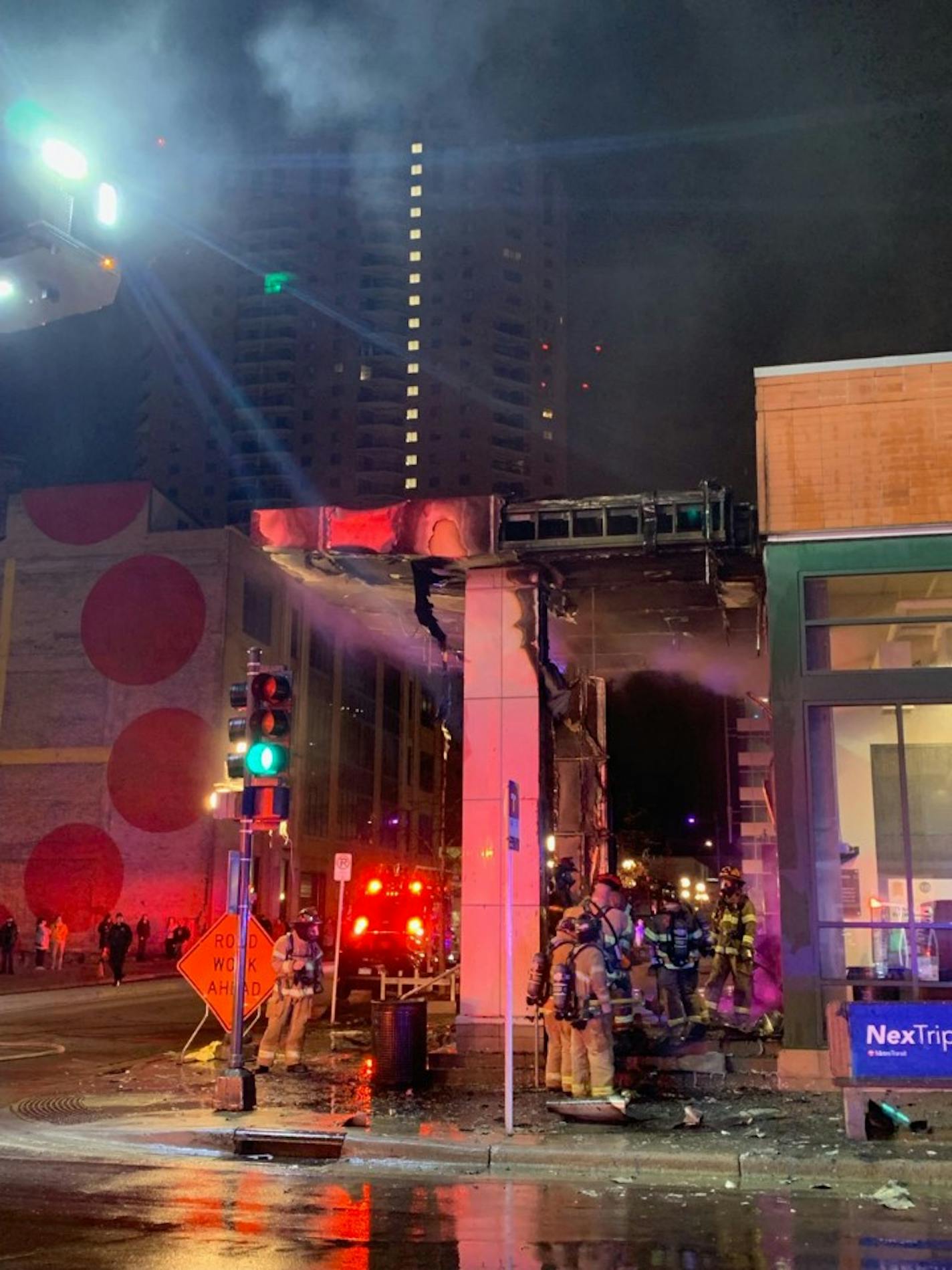 Firefighters stand around a damaged store exterior.