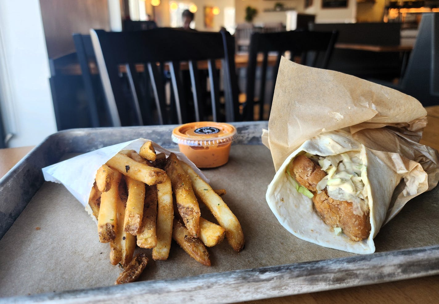 A tray with a small bag of fries, a chicken wrap in paper and a container of sauce