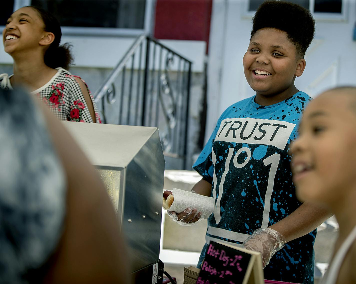 Thirteen-year-old hot dog entrepreneur Jaequan Faulkner, center, along with his cousin Destinee Grandberry, 12, left, cq, was all smiles after the city helped him bring his stand up to standards and back in business, Monday, July 16, 2018 in Minneapolis, MN. "I used to have depression," said Faulkner. "I didn't think I was good at anything," he said. Faulkner said he plans to use the money he earns for a new hot dog cart that moves, school clothes, shoes, and will contribute .25 cents from each