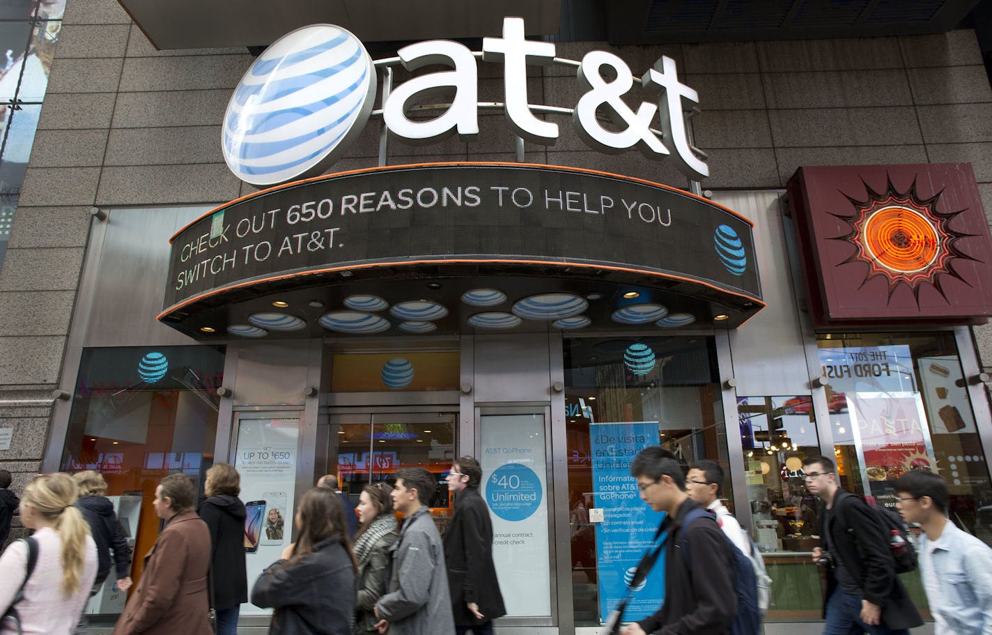 People walk by an AT&T retail store, Monday, Oct. 24, 2016, in New York. AT&T plans to buy Time Warner for $85.4 billion. (AP Photo/Mark Lennihan) ORG XMIT: MIN2016102714415727