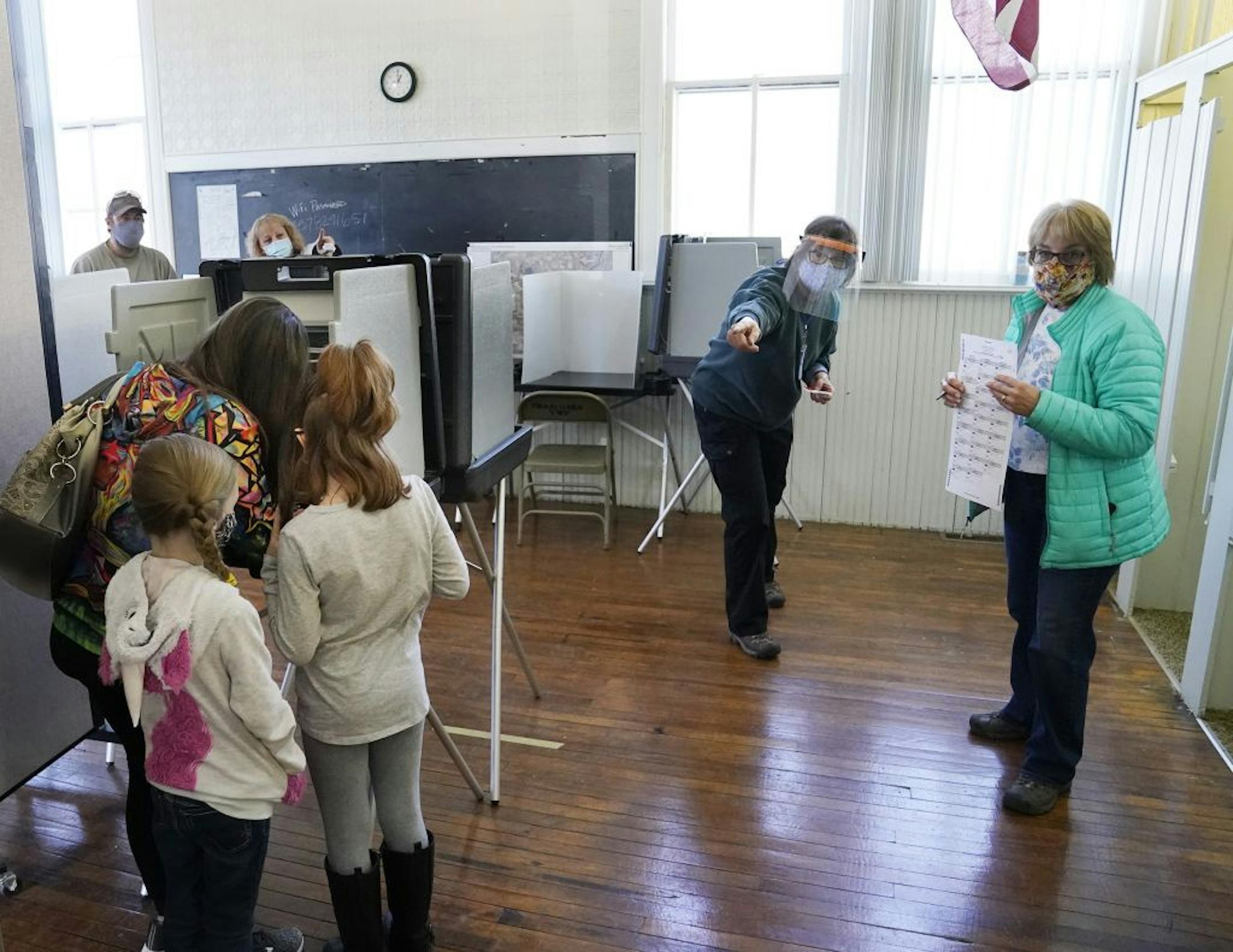Election judge Gloria Peterson, second from right, directed a voter to a counting machine as Katelyn Armstrong of Shafer voted as her daughters Lilly, 9, and Ava, 7 looked on Tuesday at Franconia Township Town Hall in Shafer.