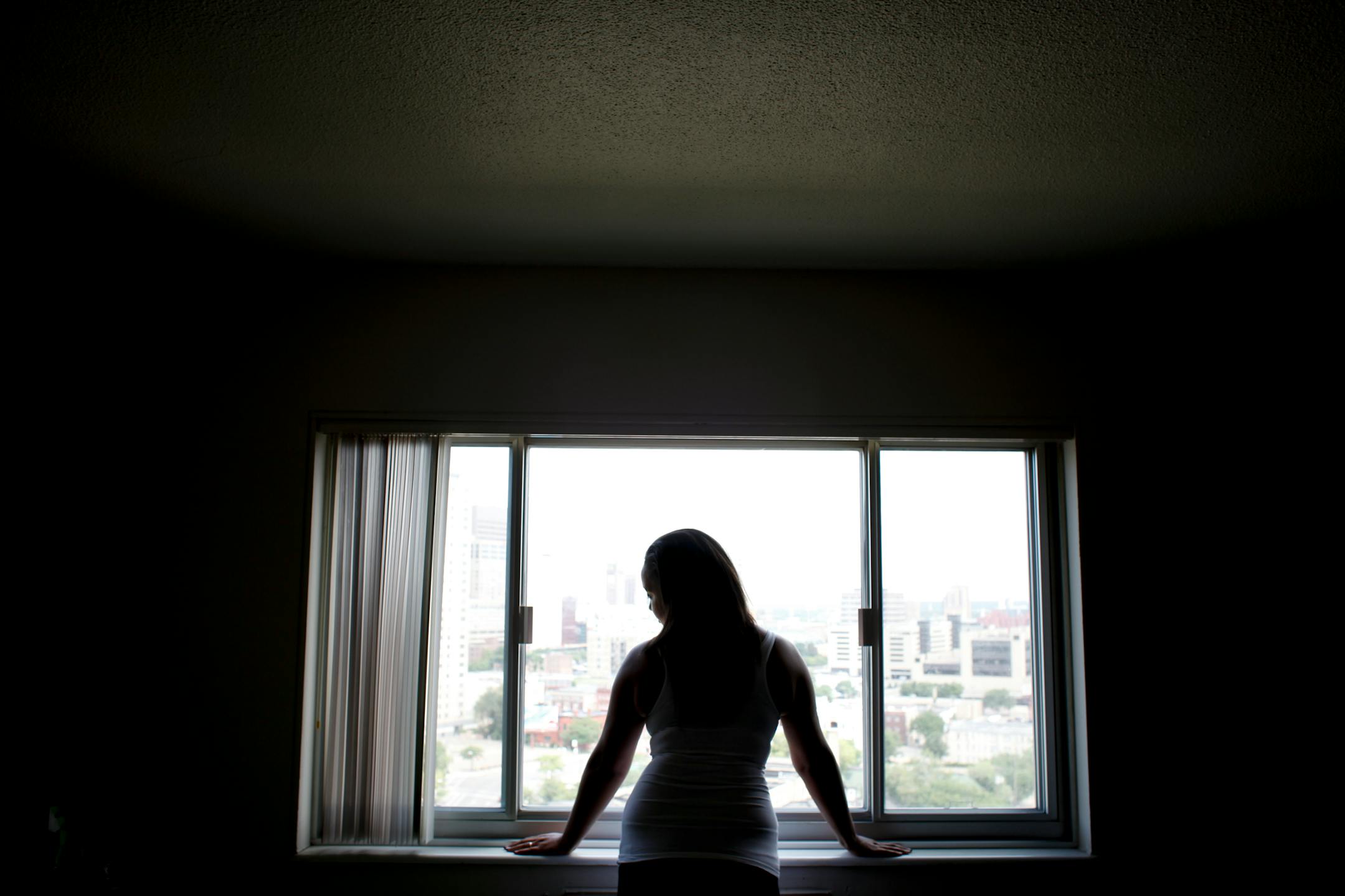 Ashely peers over the cityscape outside her apartment window in Minneapolis.