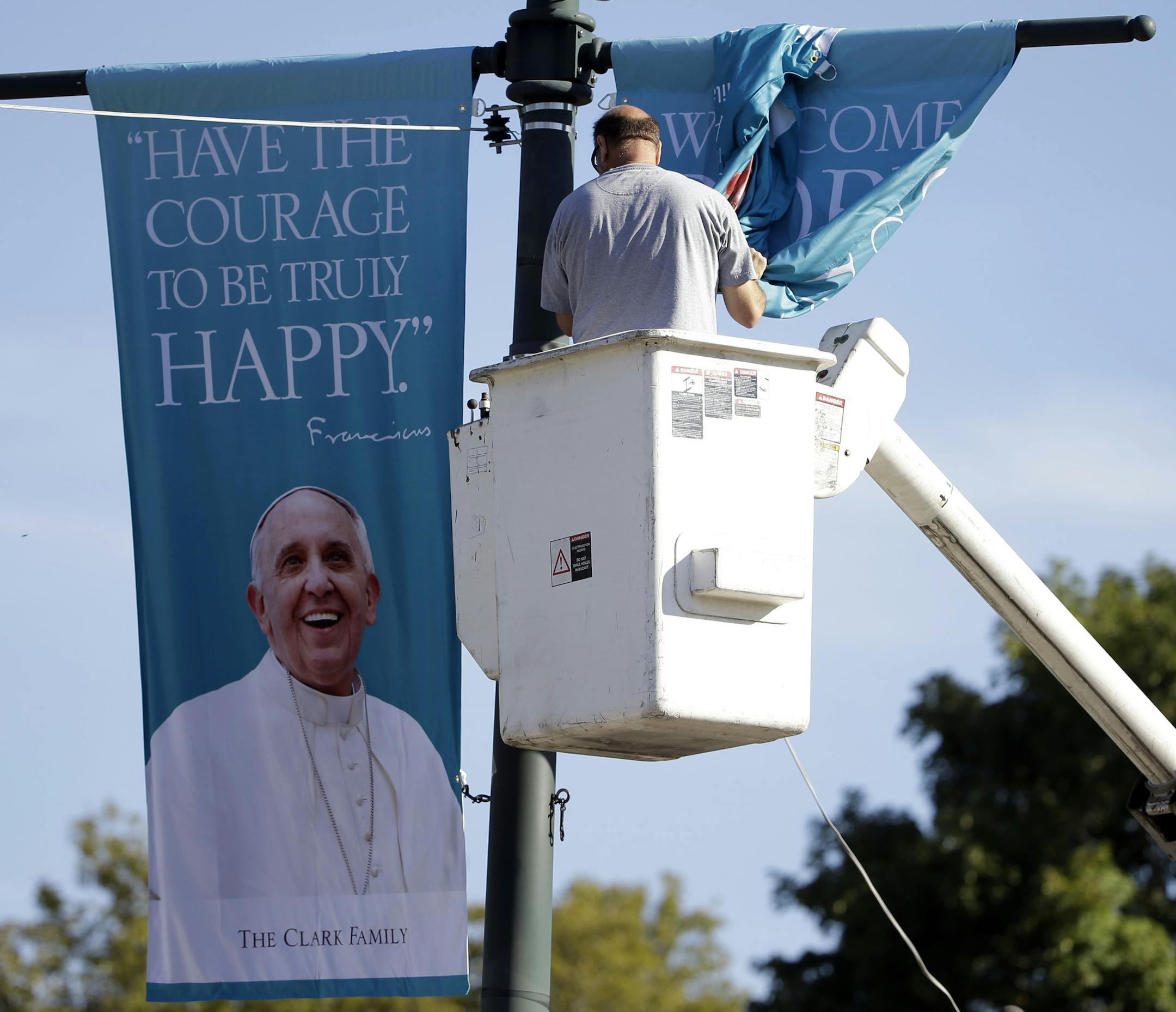 A worker hangs banners ahead of Pope Francis' scheduled visit, Wednesday, Sept. 16, 2015, on the Benjamin Franklin Parkway in Philadelphia. (AP Photo/Matt Rourke)