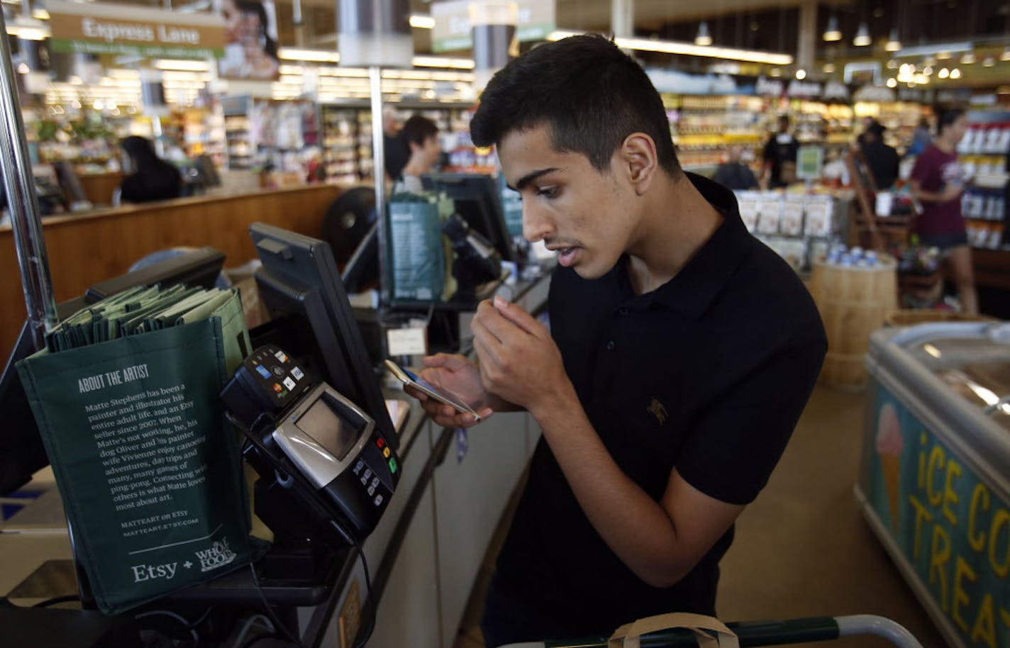 Bader Alassaf pays using Apple Pay on his iPhone 6 to purchase goods at Whole Foods Market in Dallas on Tuesday, Oct. 21, 2014. (Vernon Bryant/Dallas Morning News/MCT) ORG XMIT: 1159095