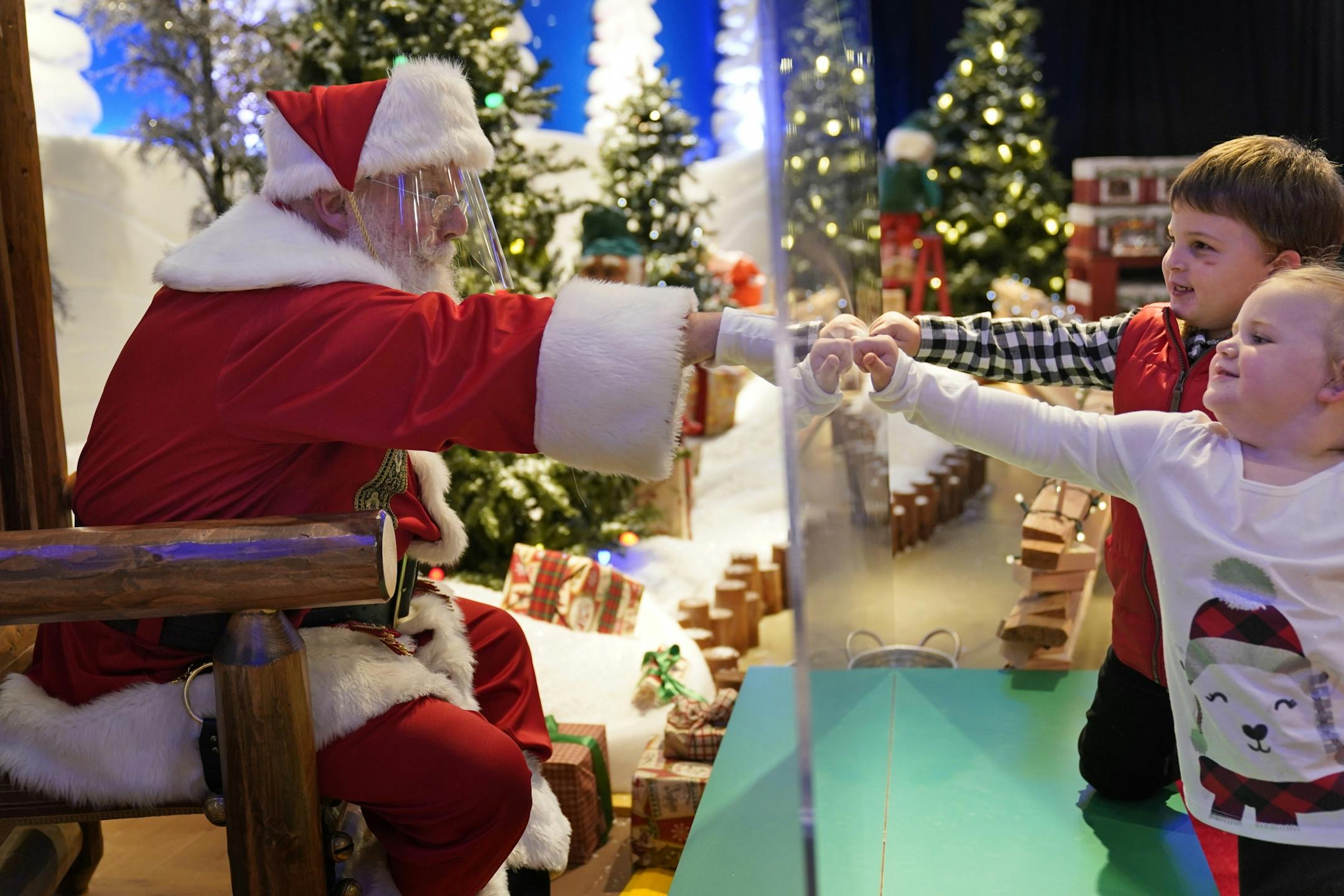 Julianna, 3, and Dylan, 5, Lasczak visit with Santa through a transparent barrier at a Bass Pro Shop in Bridgeport, Conn., Tuesday, Nov. 10, 2020. Santa Claus is coming to the mall — just don't try to sit on his lap. Malls are doing all they can to keep the jolly old man safe from the coronavirus, including banning kids from sitting on his knee, no matter if they've been naughty or nice.
