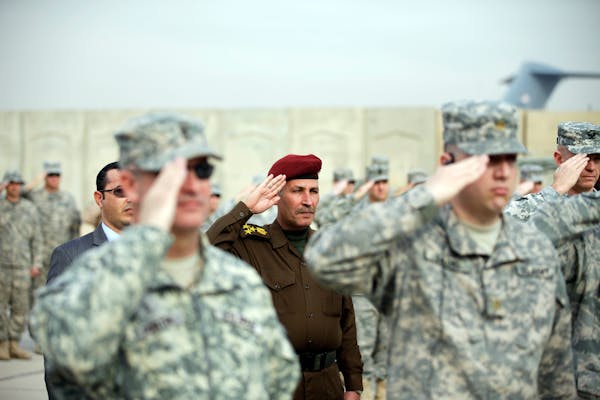 An Iraqi officer, center, and US Army soldiers salute during ceremonies marking the end of the US military mission in Baghdad, Iraq, Thursday, Dec. 15