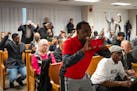 Mohamed Said, an Uber/Lyft driver, uses a phone to record the Minneapolis City Council meeting as people behind him begin to cheer just after the coun