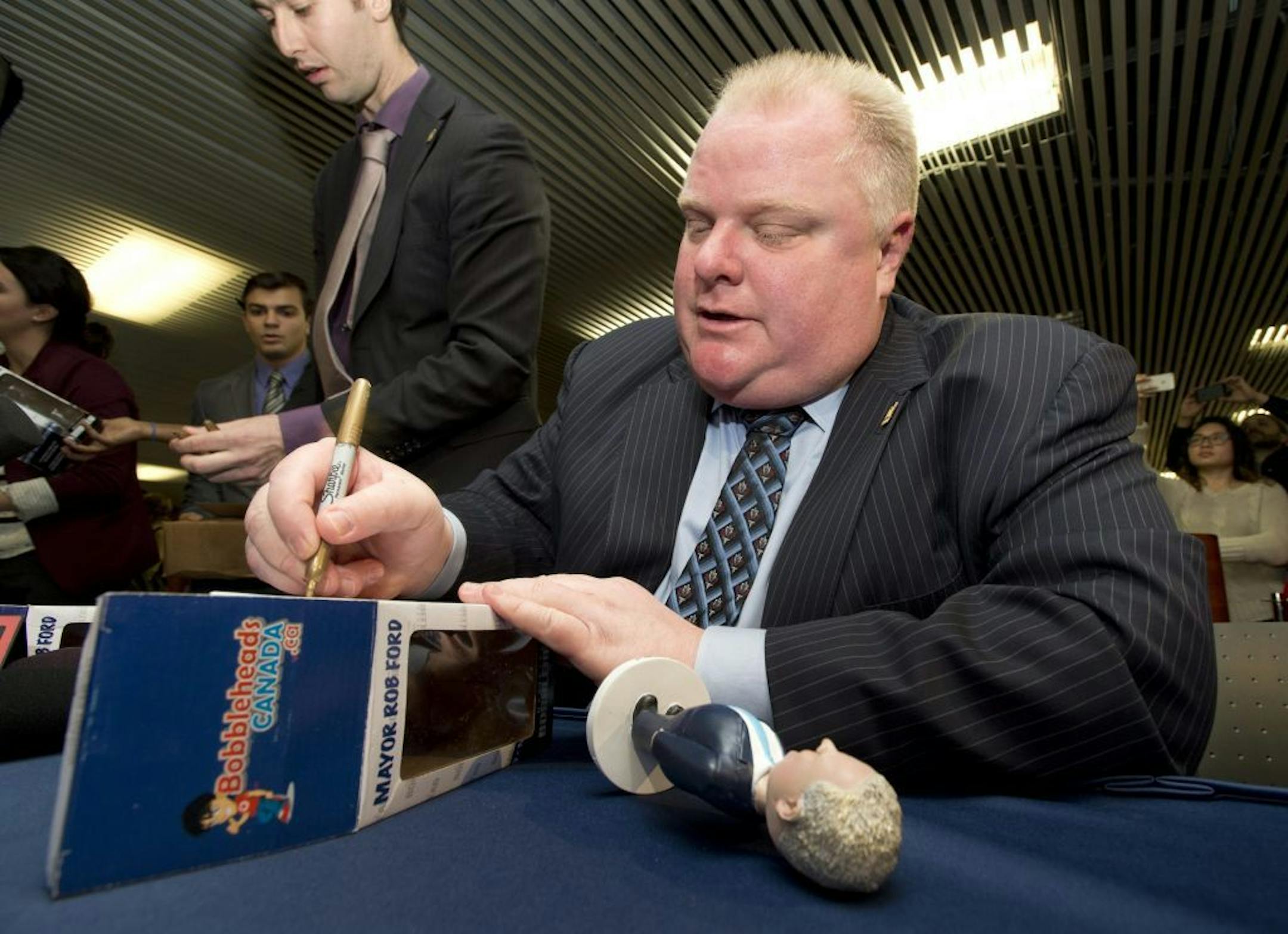 Toronto Mayor Rob Ford autographs the box of a bobblehead doll in his likeness Tuesday, Nov. 12, 2013, at city hall in Toronto. Hundreds of people lined up to be the first to own the bobblehead doll, with proceeds going to charity.