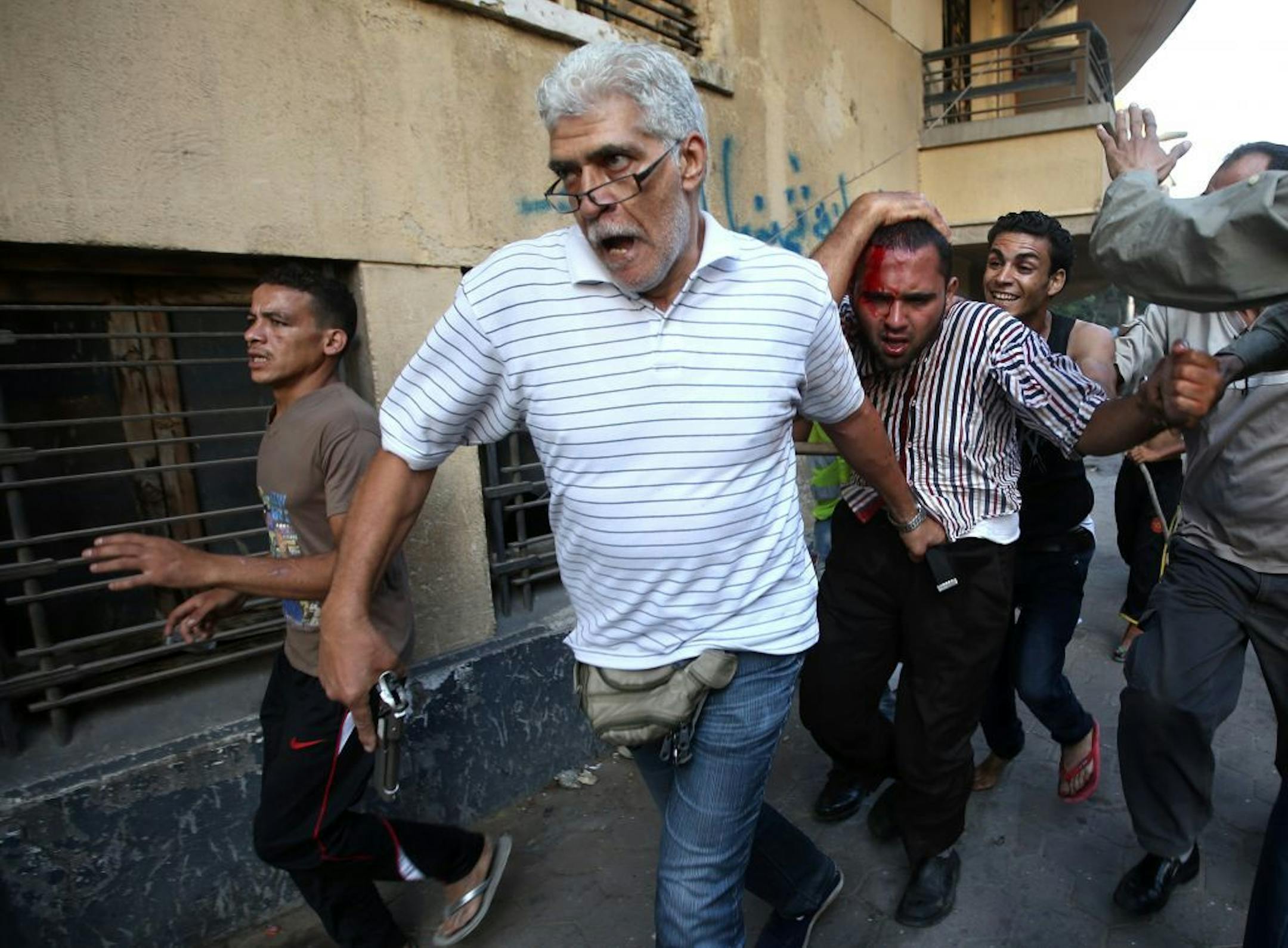 An Egyptian man with a pistol, second left, and opponents of Egypt's ousted President Mohammed Morsi, detain a suspected Morsi supporter who was wounded during clashes in Cairo, Monday, July 22, 2013.