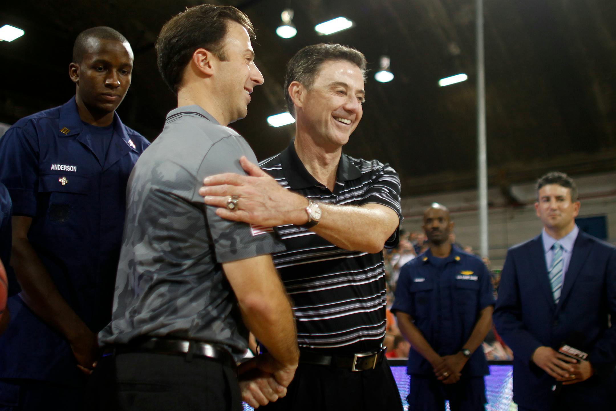 Minnesota head coach Richard Pitino, front left, greets his father, Louisville head coach Rick Pitino, before the start of their NCAA college basketball Armed Forces Classic game inside a hangar at the United States Coast Guard Air Station base in Aguadilla, Puerto Rico, Friday, Nov. 14, 2014. (AP Photo/Ricardo Arduengo)