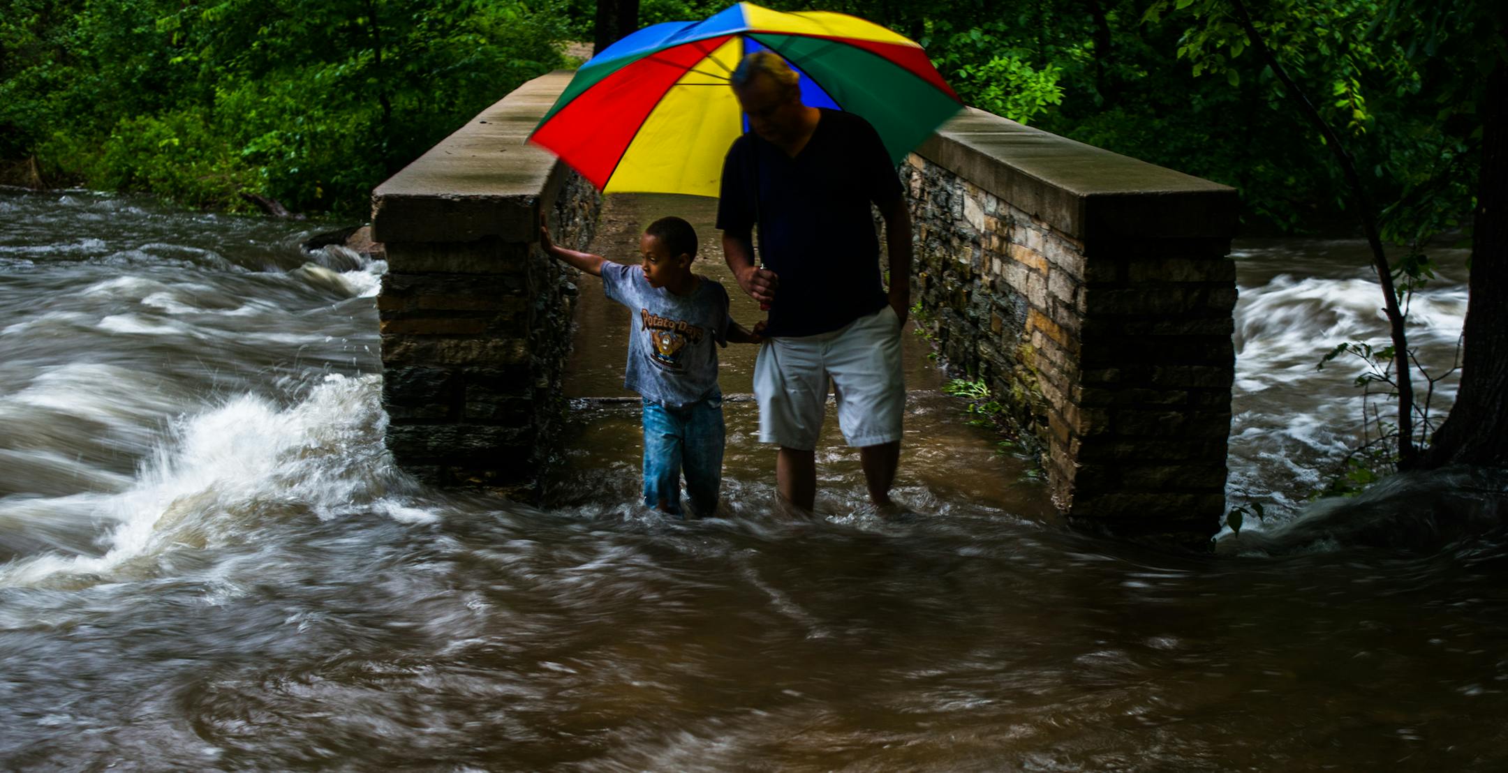 [ MARK VANCLEAVE * mark.vancleave@startribune.com * WX062014 * 262621 Heavy rain caused flooding along Minnehaha Creek in Minneapolis on Thursday, Jun 19, 2014. rain weather minneapolis storm flood minnesota ] Craig Susag and his grandson Nethaniel cross a flooded bridge over Minnehaha Creek in Minnehaha Park.