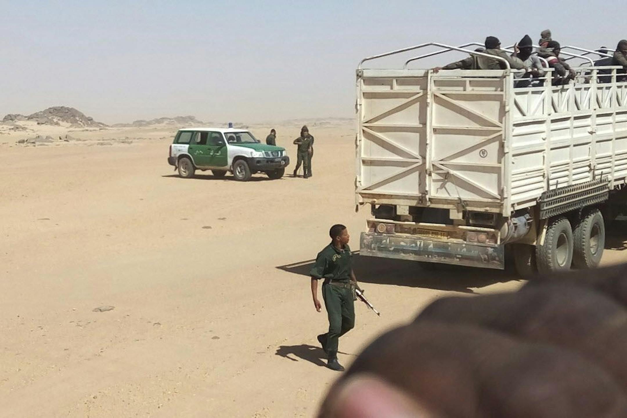 In this Tuesday, May 8, 2018 photo provided by Liberian migrant Ju Dennis, Algerian gendarmes carrying AK-47 assault rifles load migrants onto trucks to drop them off at the Niger border. Algeria has abandoned more than 13,000 people in the desert in the past 14 months, including pregnant women and children, stranding them without food or water and forcing them to walk, sometimes at gunpoint, under temperatures of up to 48 degrees Celsius (118 degrees Fahrenheit). Dennis filmed his deportation w
