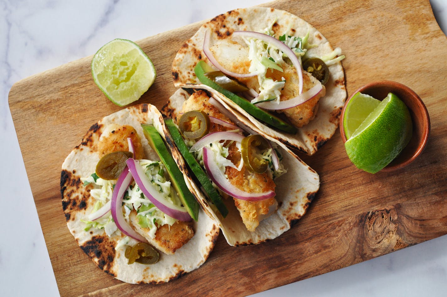 Three Pan-Fried Crispy Fish Tacos with Creamy Cilantro Slaw on a wooden cutting board.