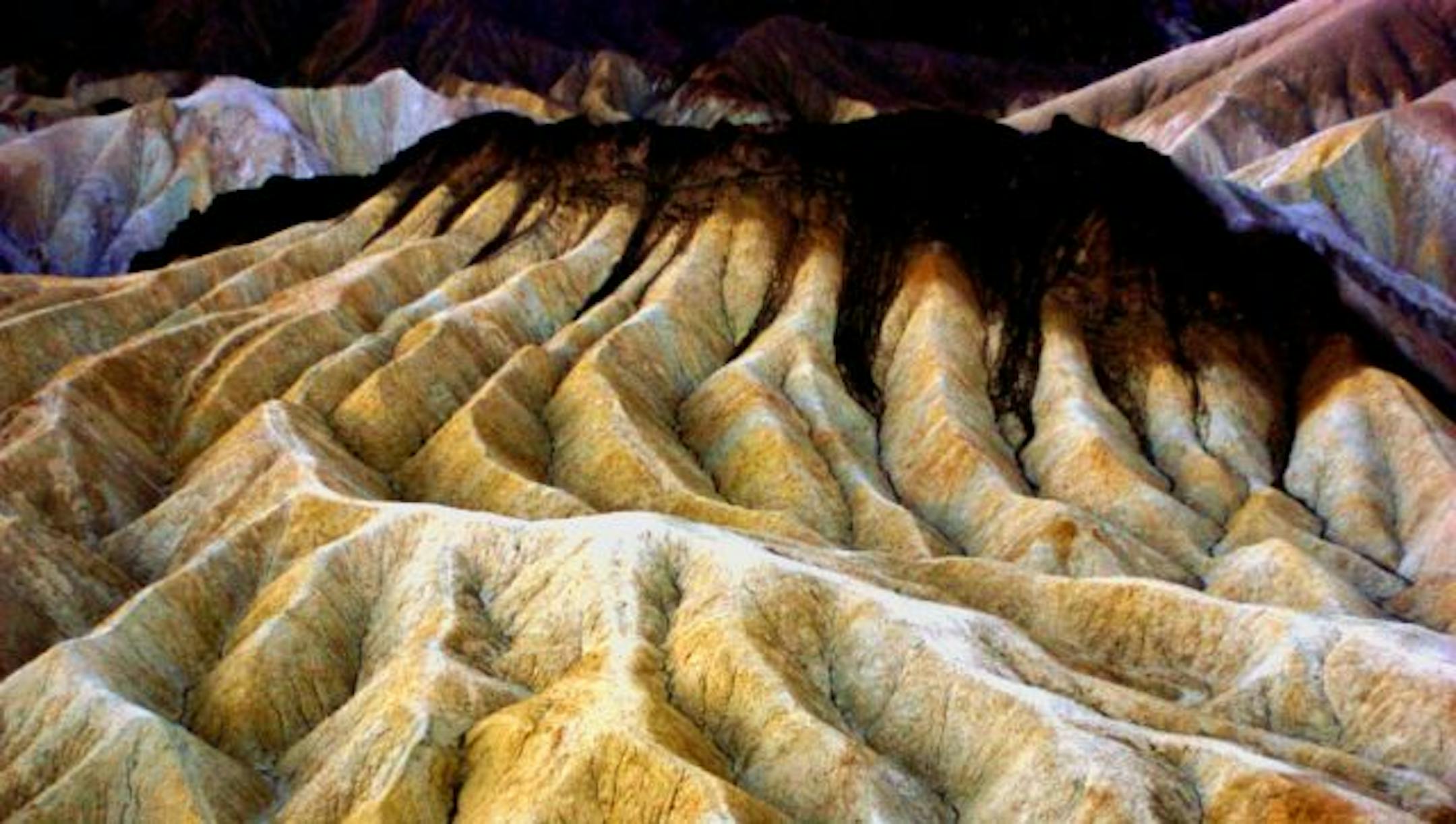 Eroding badland sediments colored by iron and other minerals glow golden under a setting sun at Zabriski Point, one of the most popular and spectacular vista points in Death Valley National Park.