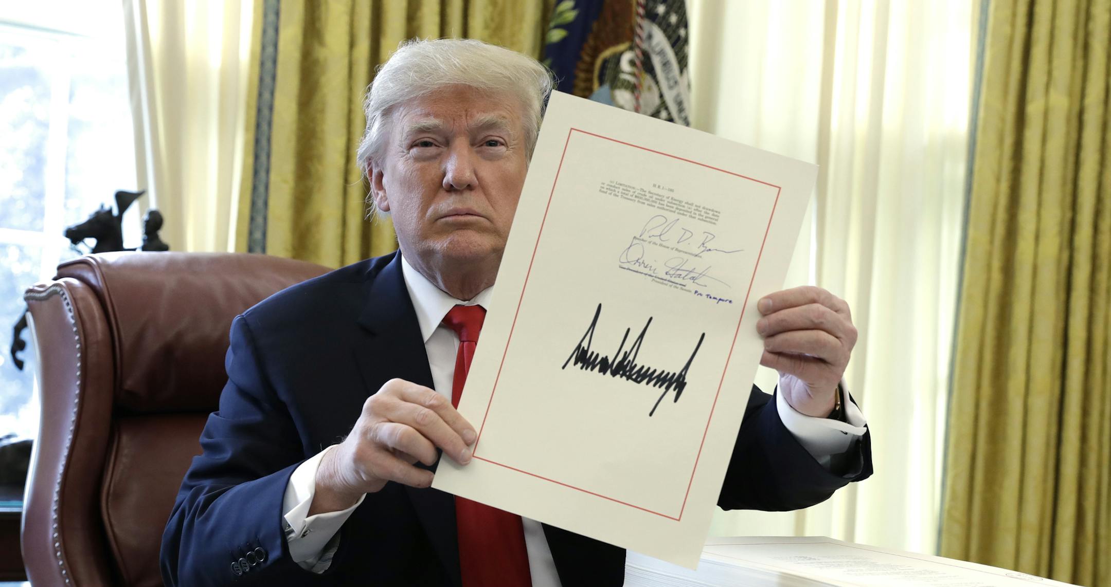 President Donald Trump displays the $1.5 trillion tax overhaul package he had just signed, Friday, Dec. 22, 2017, in the Oval Office of the White House in Washington. Trump touted the size of the tax cut, declaring to reporters in the Oval Office before he signed it Friday that "the numbers will speak." (AP Photo/Evan Vucci)