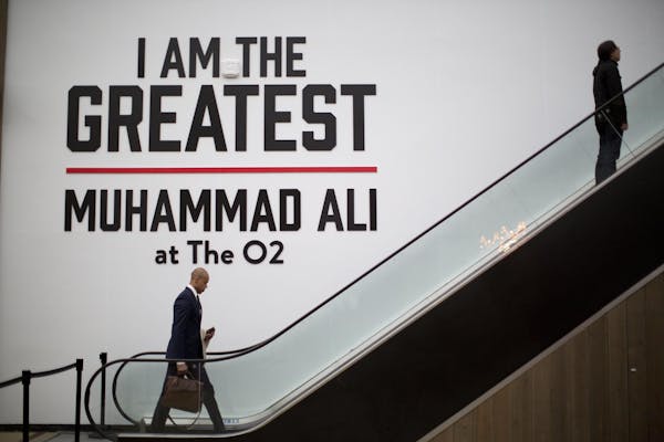 Men pass a large sign by an escalator near the entrance of the "I Am The Greatest, Muhammad Ali" exhibition at the O2 arena, which hosts high profile 