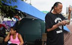 Yvonne, 32, sits in the makeshift camp just off of Hiawatha and Cedar Avenues as James Cross, founder of Natives Against Heroin, burns sage and prays 