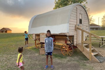 The author’s granddaughters check into a covered wagon available for an overnight stay at the Ingalls Homestead in De Smet, S.D.