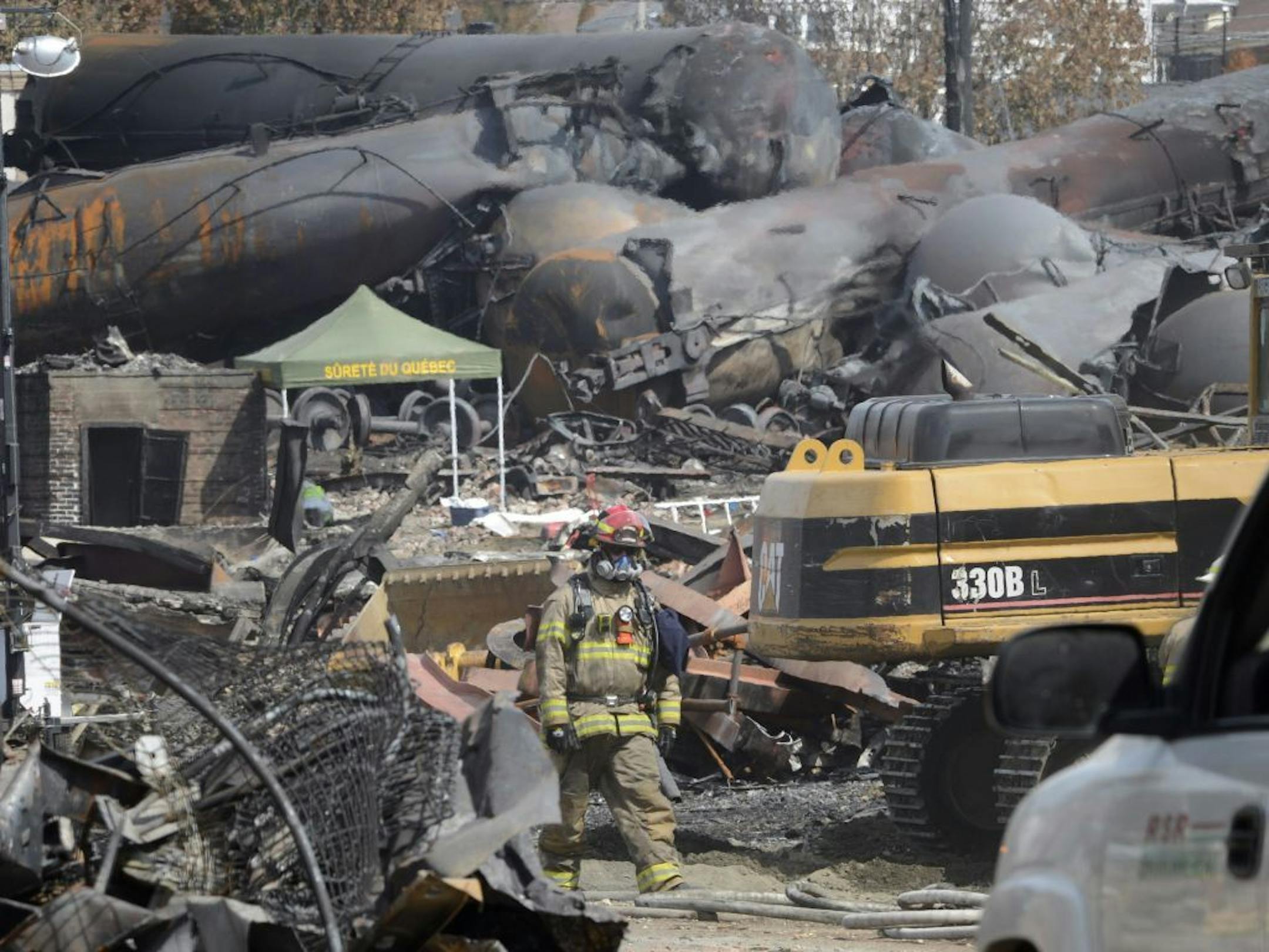 Wearing protective gear an emergency worker moves though the wreckage of the oil train derailment and explosion in in Lac-Megantic, Qiuebec, on Tuesday, July 16, 2013. Thirty-seven bodies have been recovered and another thirteen people are missing from the July 6, 2013, accident.