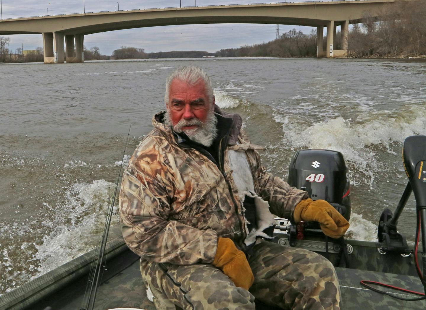 With the Interstate 494 bridge in the background, Dick "Griz'' Grzywinski guides his john boat downriver on the Mississippi. Sunny for a while, the fishing day Grzywinski and Dennis Anderson chose was chilly and soon overcast.