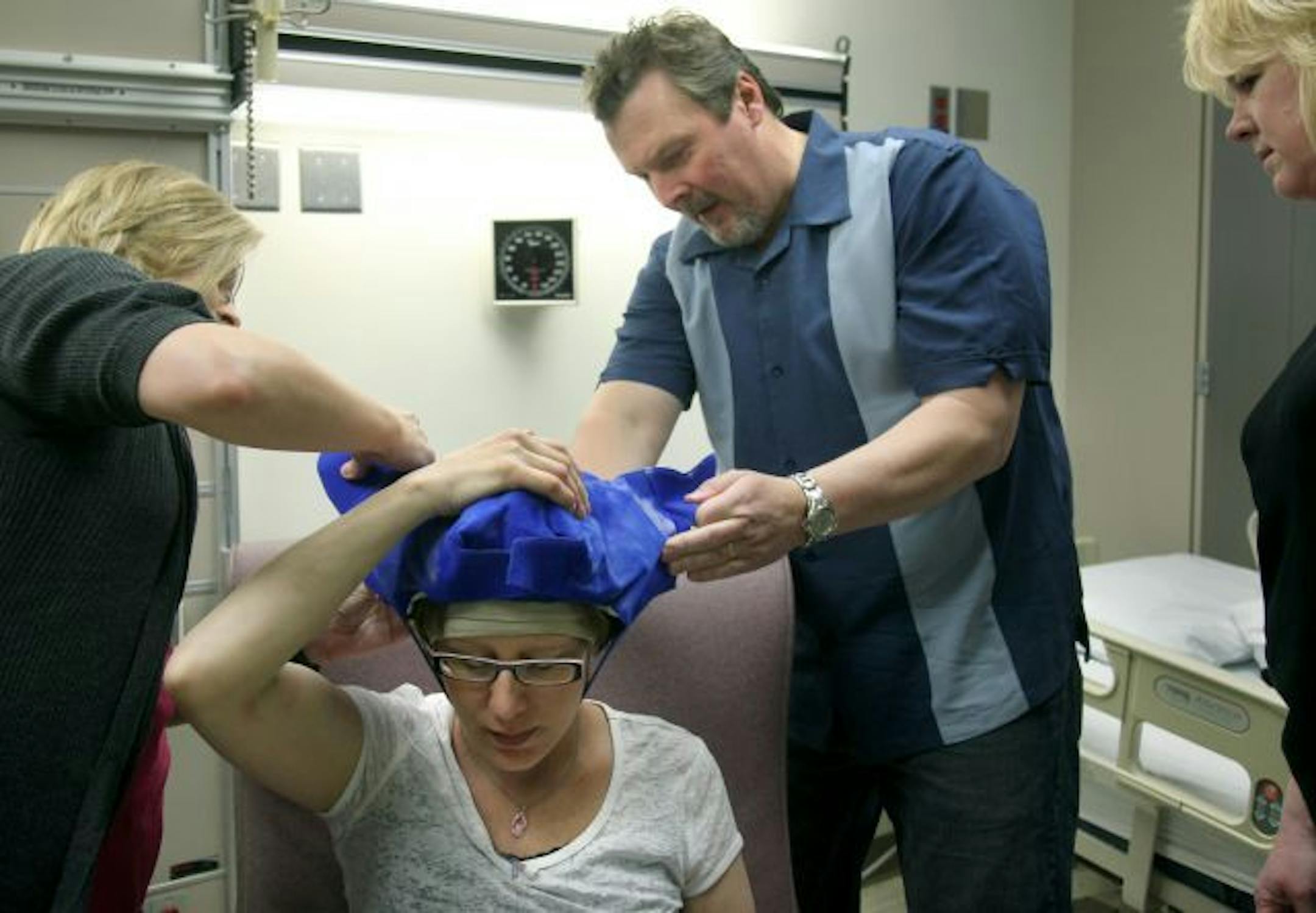 Chris Greene, took a placed a chilled cap on his wife Carrie Greene, as she received chemotherapy treatment. Her husband Chris was there to show Greene's friends, Kris Olson, left, and Barb Thomson, right, how to prepare the chilled caps.