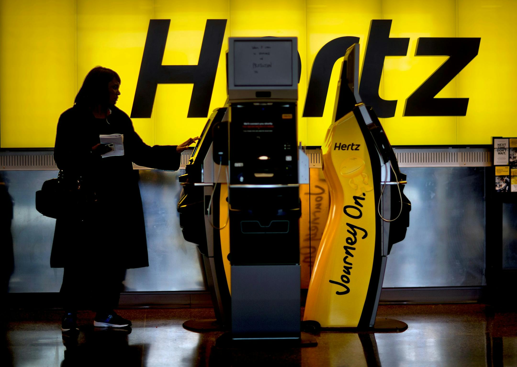 FILE - In this Nov. 27, 2013, file photo, a customer checks in at a Hertz car rental counter at Hartsfield-Jackson Atlanta International Airport, in Atlanta. Hertz reports financial results on Monday, Aug. 8, 2016. (AP Photo/David Goldman, File) ORG XMIT: NYBZ123