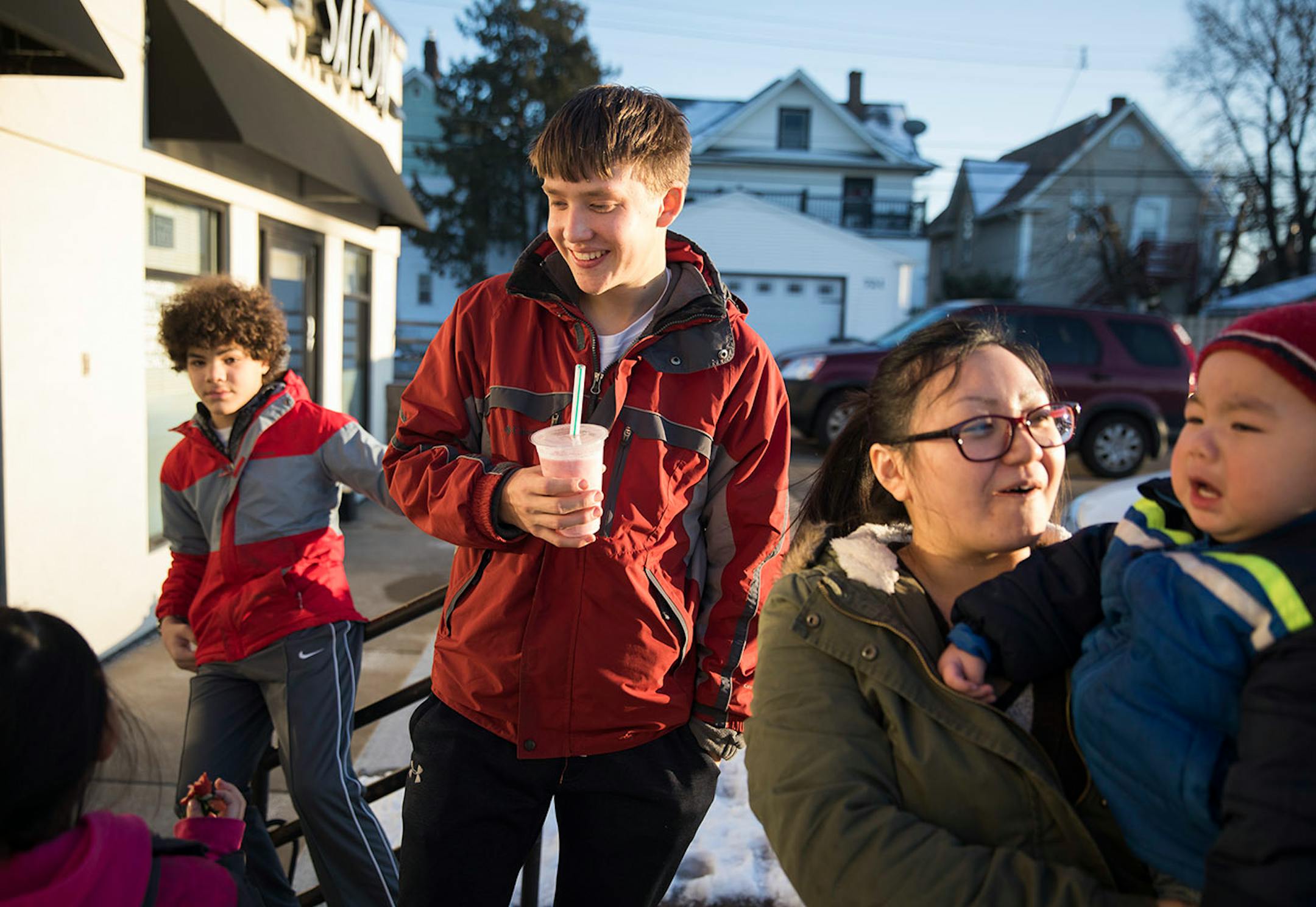 Minnehaha Academy students Daniel Rose, from left, 14, and Peter Shaffer, 14, enjoy fruit smoothies outside a fruit shop off University Avenue in St. Paul with their host See Vue and her 18-month-old son Raj. ] LEILA NAVIDI ï leila.navidi@startribune.com BACKGROUND INFORMATION: in St Paul on Wednesday, March 15, 2017. City Stay is an opportunity for Minnesota high school students to do home stays at the homes of other local residents. The cultural exchange program fosters new relationships among