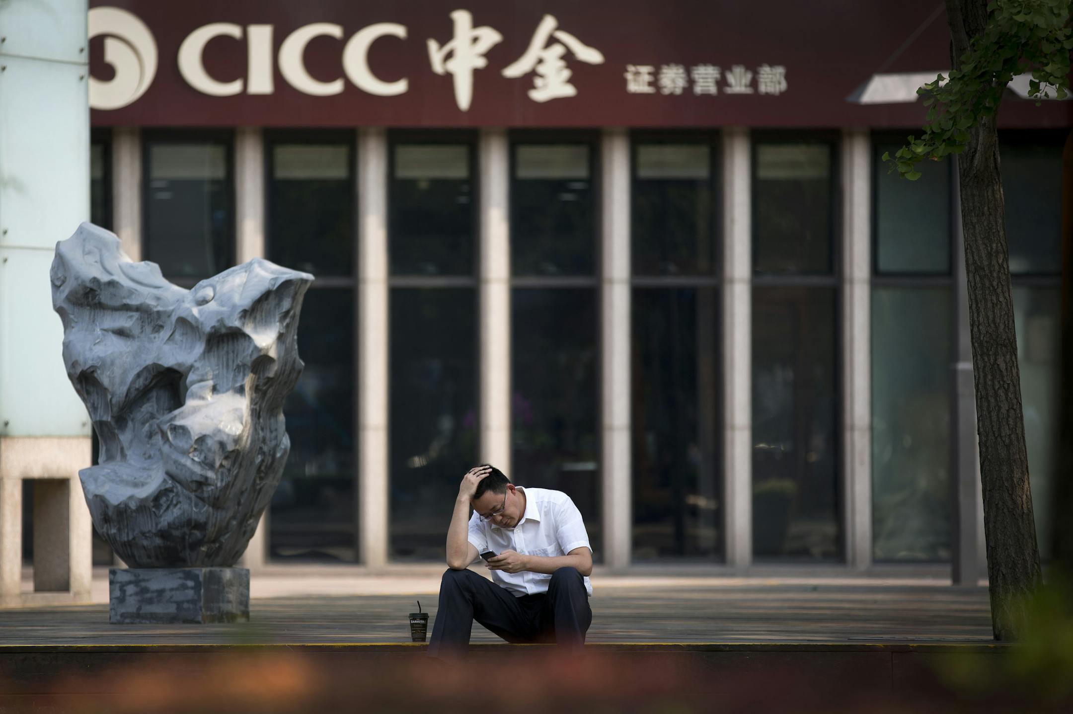 A man rubs his head while browsing his smartphone outside a brokerage house in Beijing Tuesday, July 7, 2015. Chinese stocks fell Tuesday despite official efforts to shore up slumping prices while other Asian markets were mixed after Greece's spiraling crisis weighed on Wall Street. (AP Photo/Andy Wong)