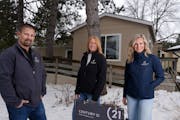 Real estate agents Nate Campion, Tricia Anderson, and Carrie Gibbs with Century 21 Moline Realty stand for a portrait outside a manufactured home Camp